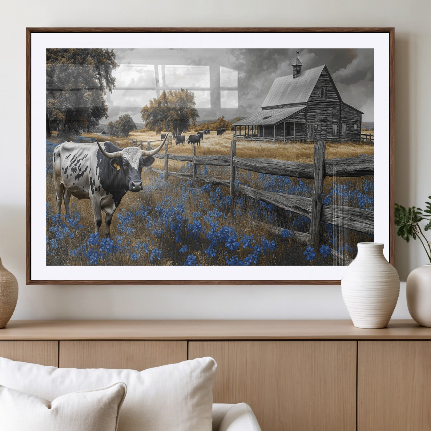 A Texas longhorn stands in front of a rustic barn and wooden fence, with bluebonnets and grazing cattle under dramatic skies.