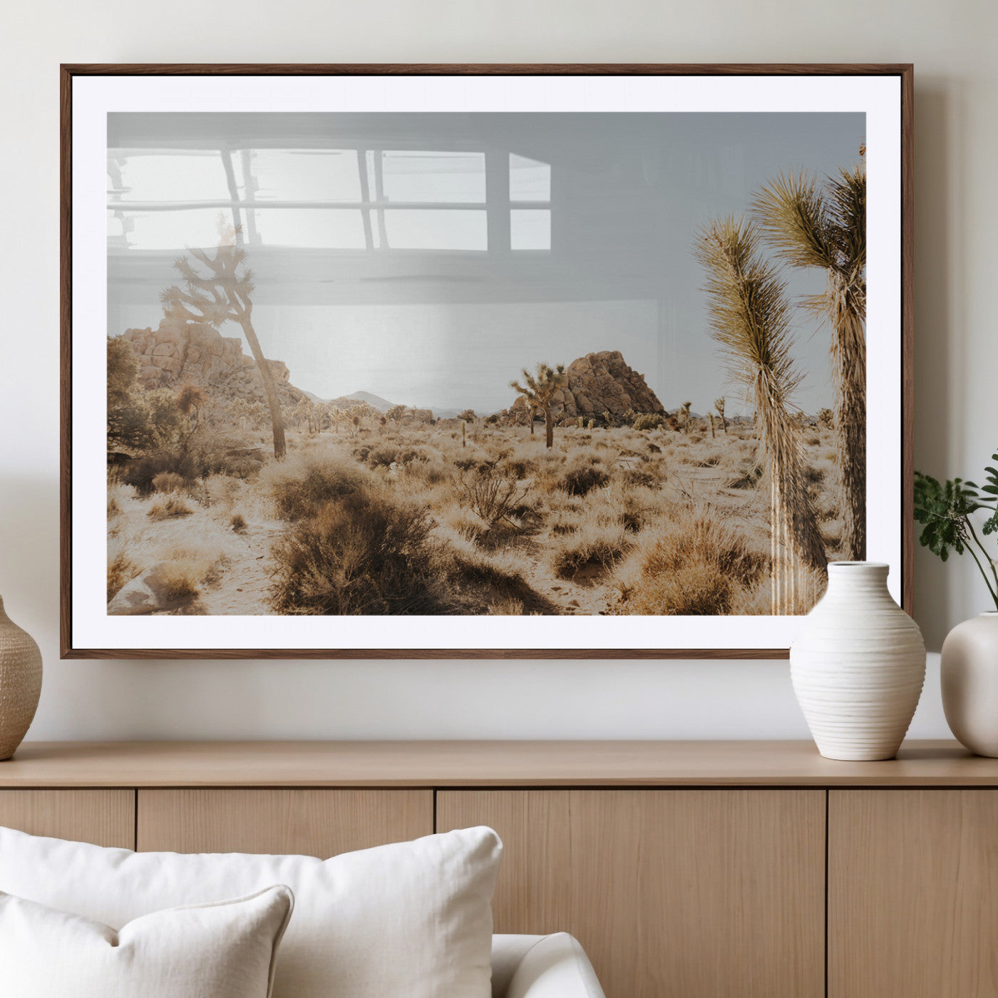 Sunlit desert landscape featuring Joshua trees, rocky formations, and dry bushes under a clear sky.