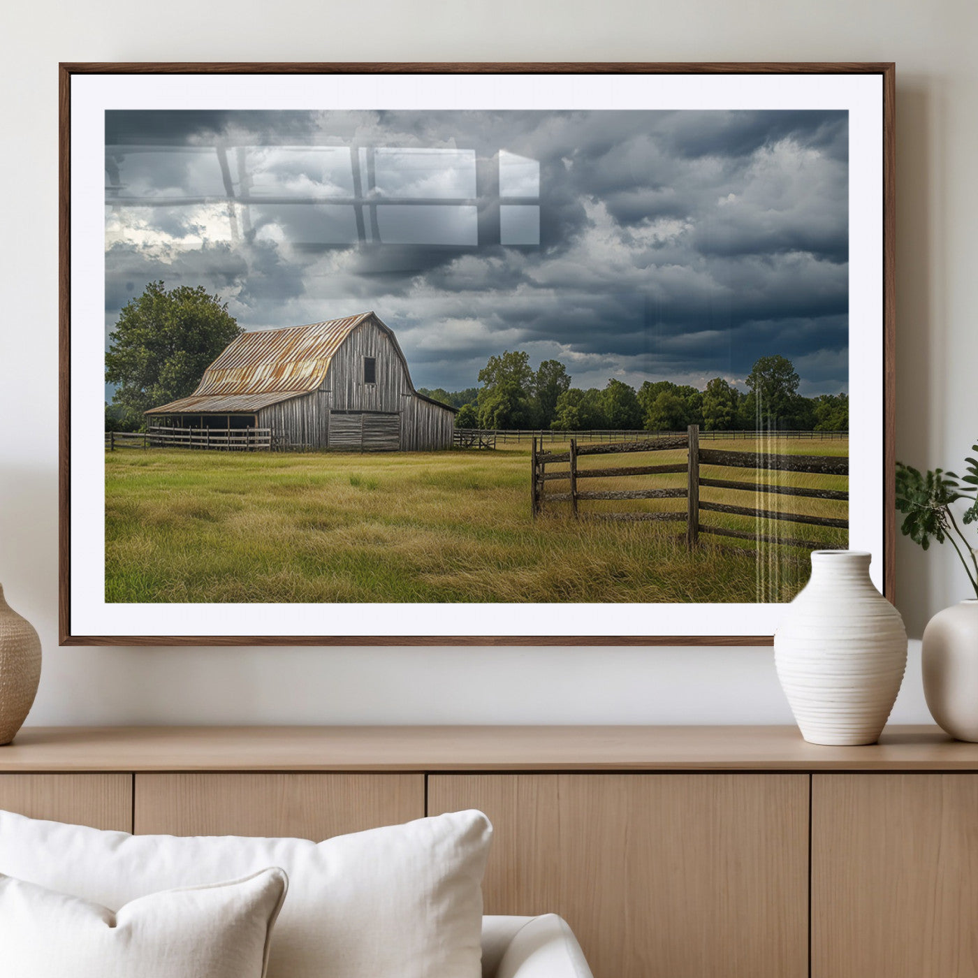 "Rustic barn in a wide open field under a dramatic sky with dark clouds, surrounded by a wooden fence and lush green trees."