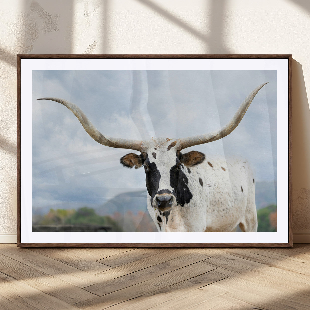 Close-up of a Texas Longhorn with curved horns, black and white markings, set against a cloudy sky and distant hills, perfect for rustic decor.