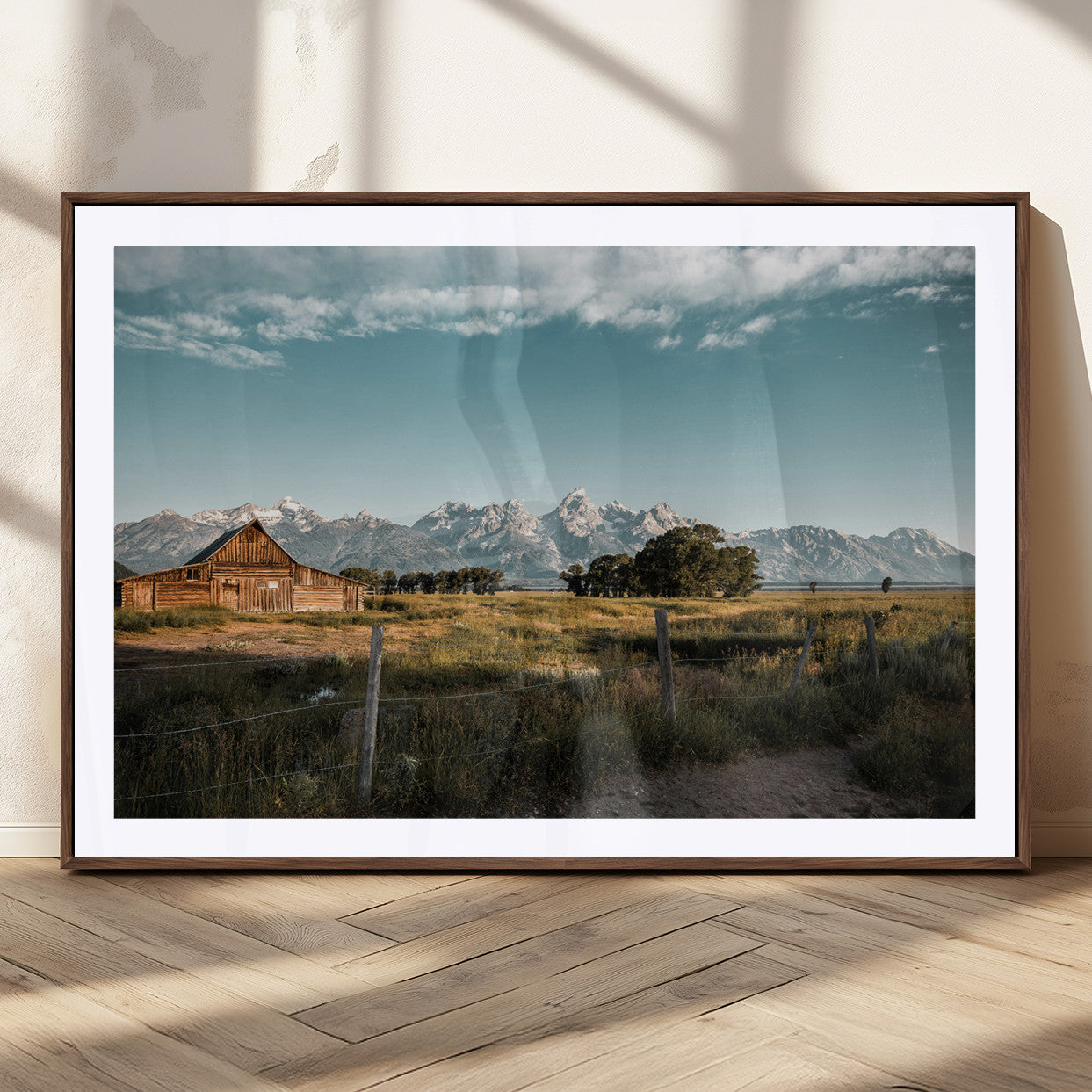 A rustic farmhouse with a wooden barn set against majestic mountain peaks under a soft blue sky, evoking peaceful countryside charm.