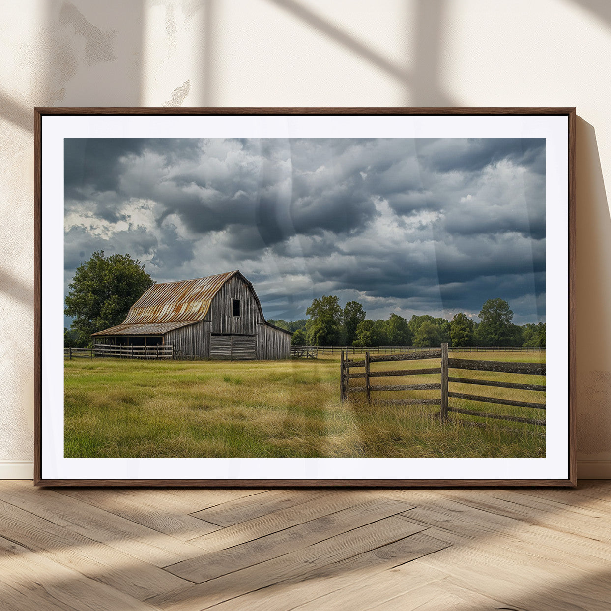"Rustic barn in a wide open field under a dramatic sky with dark clouds, surrounded by a wooden fence and lush green trees."