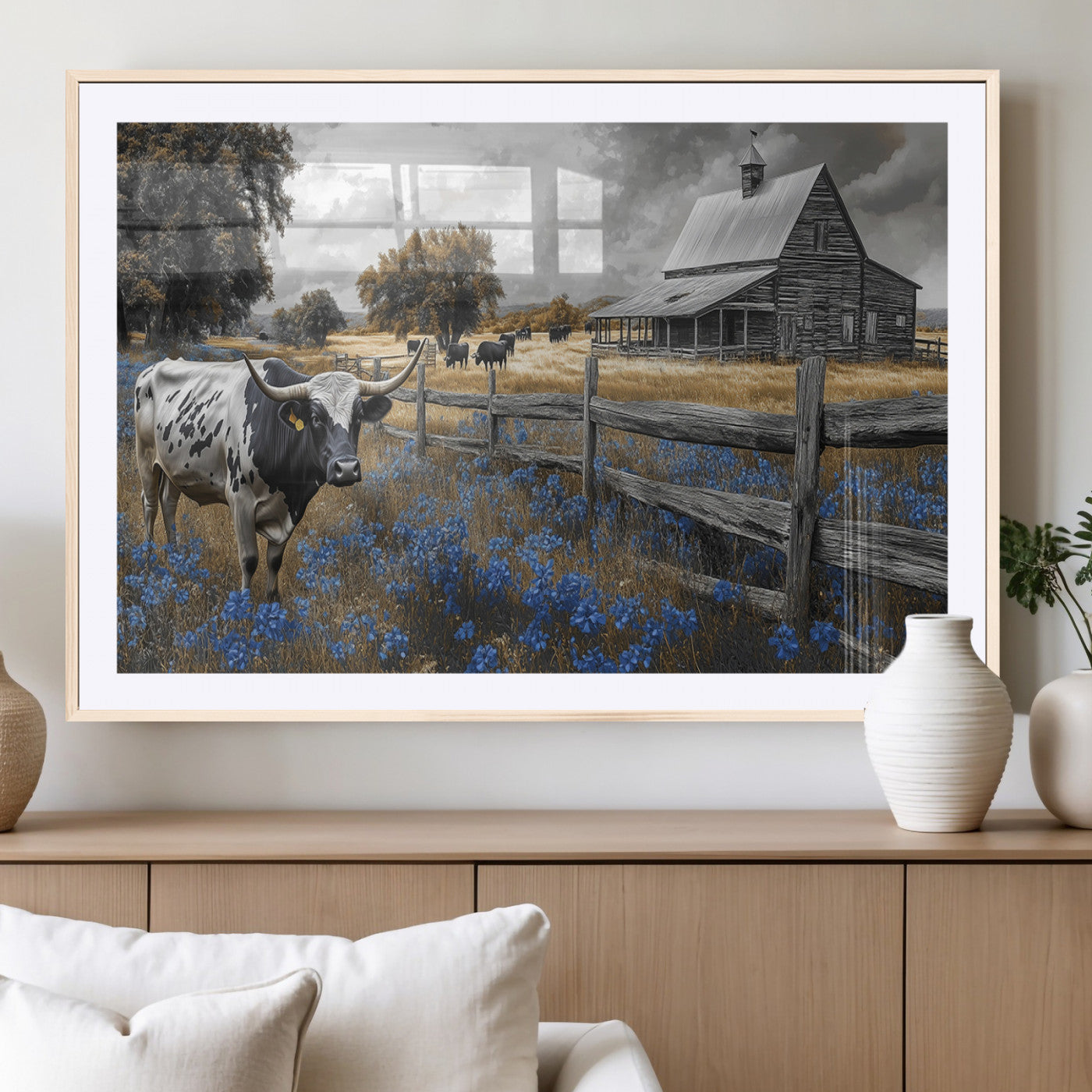 A Texas longhorn stands in front of a rustic barn and wooden fence, with bluebonnets and grazing cattle under dramatic skies.