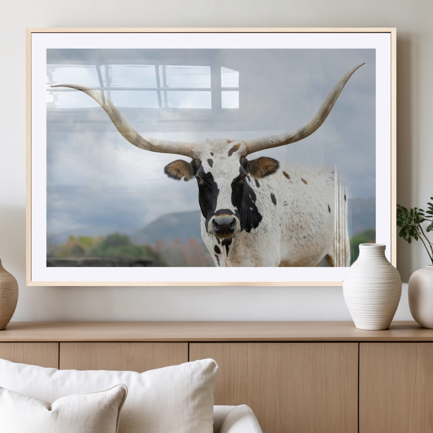 Close-up of a Texas Longhorn with curved horns, black and white markings, set against a cloudy sky and distant hills, perfect for rustic decor.