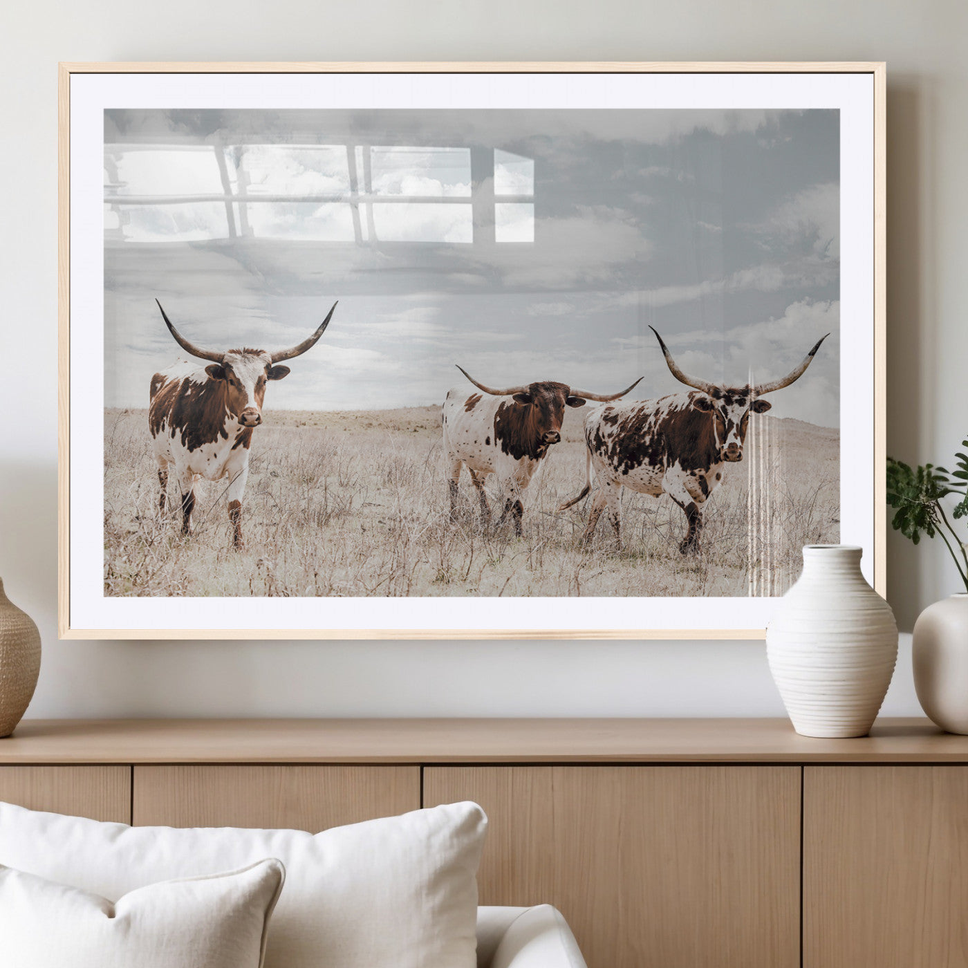 Three Texas Longhorn cattle walking through a dry grassy field under a partly cloudy sky.