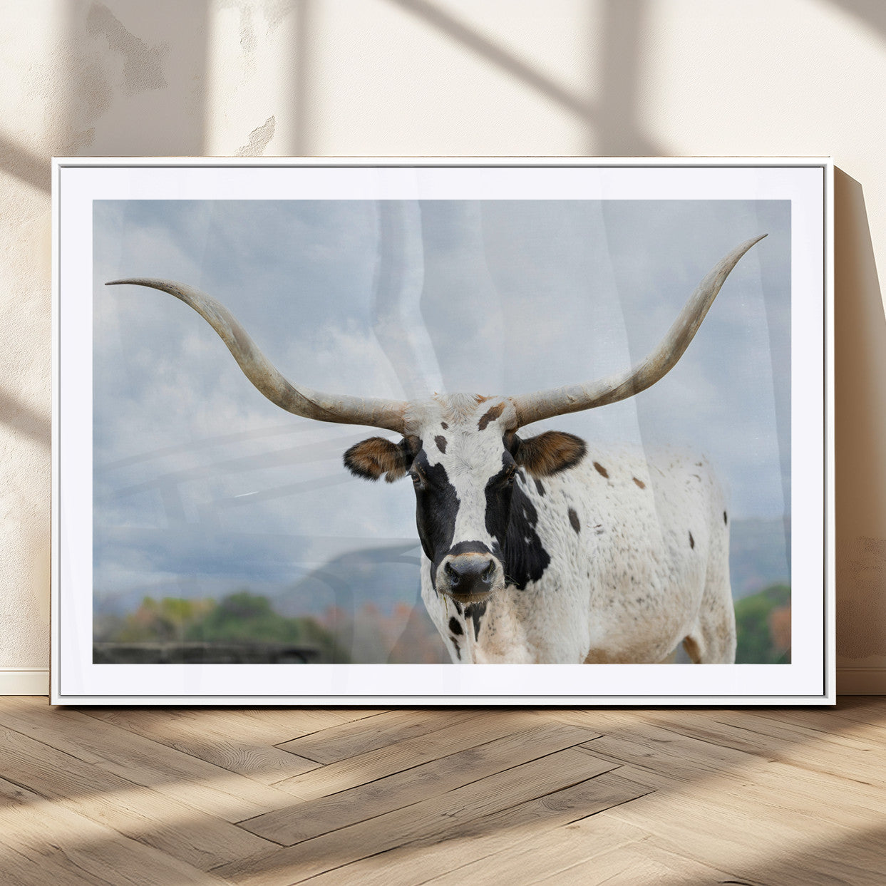 Close-up of a Texas Longhorn with curved horns, black and white markings, set against a cloudy sky and distant hills, perfect for rustic decor.