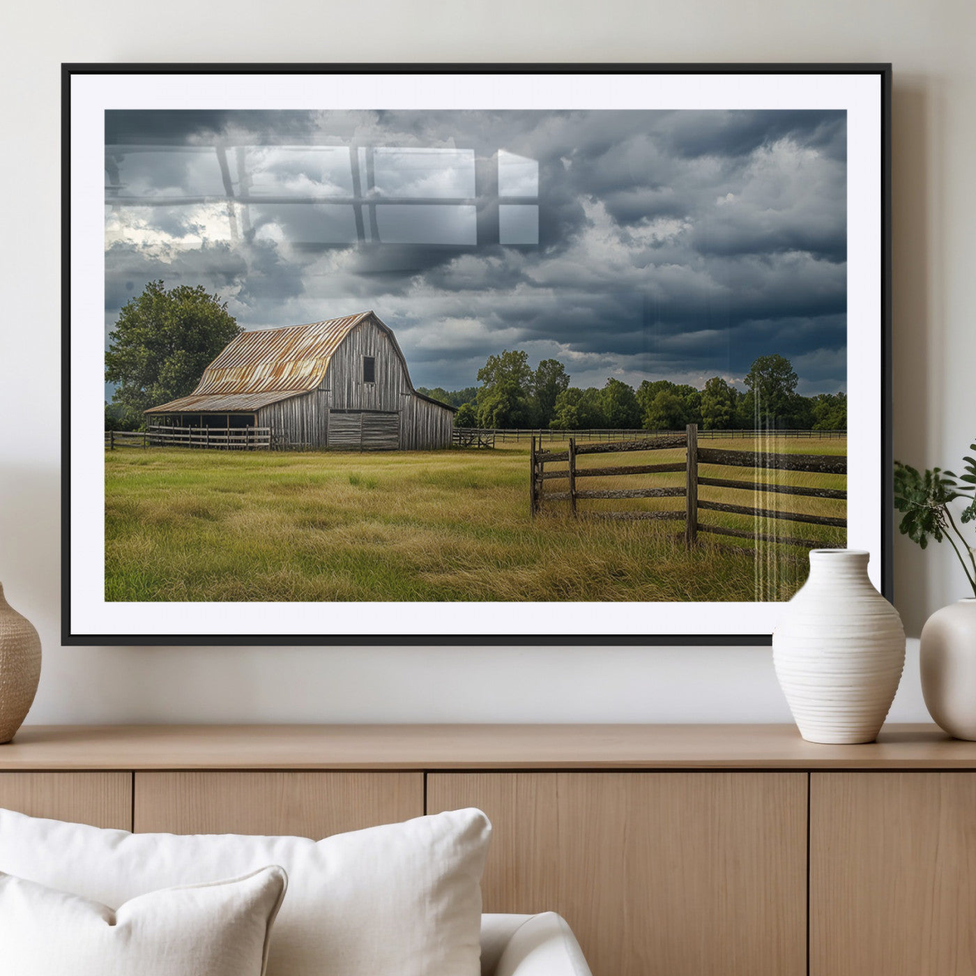 "Rustic barn in a wide open field under a dramatic sky with dark clouds, surrounded by a wooden fence and lush green trees."