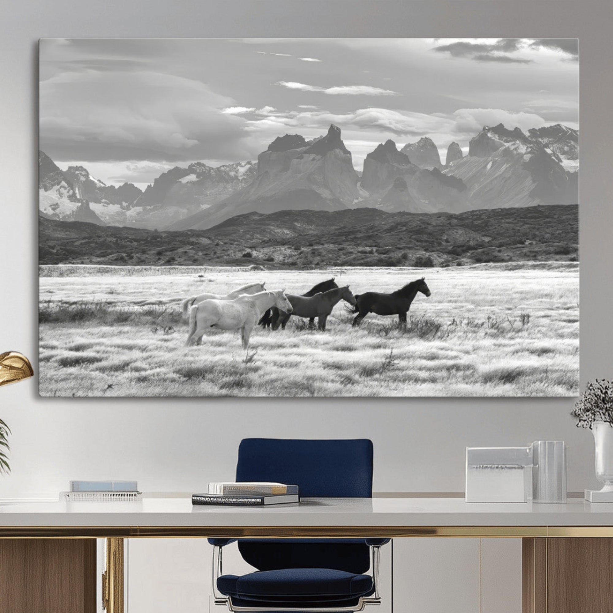 A black and white landscape of wild horses grazing in a vast grassland with towering mountains in the background, creating a moody and rustic western aesthetic.