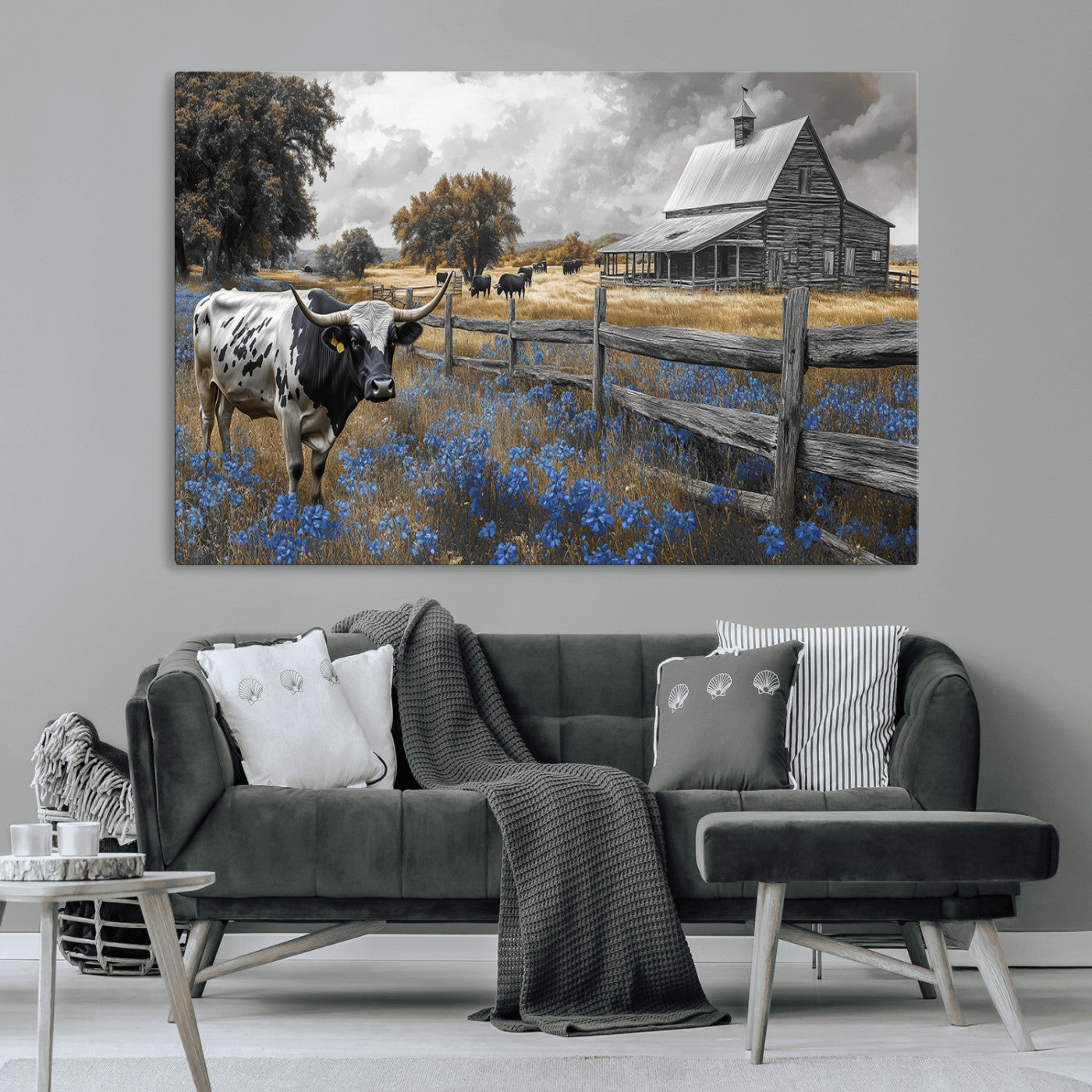 A Texas longhorn stands in front of a rustic barn and wooden fence, with bluebonnets and grazing cattle under dramatic skies.