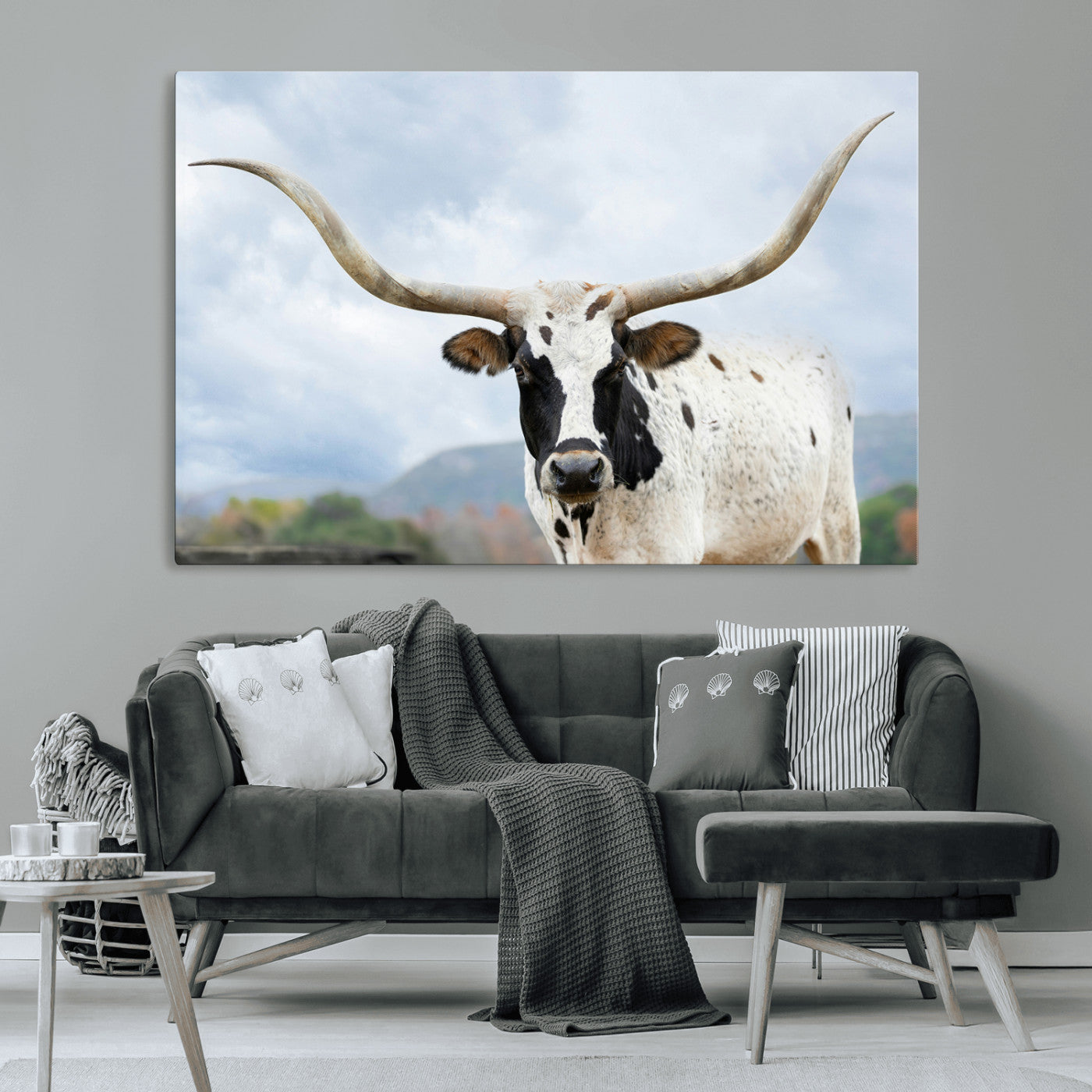 Close-up of a Texas Longhorn with curved horns, black and white markings, set against a cloudy sky and distant hills, perfect for rustic decor.