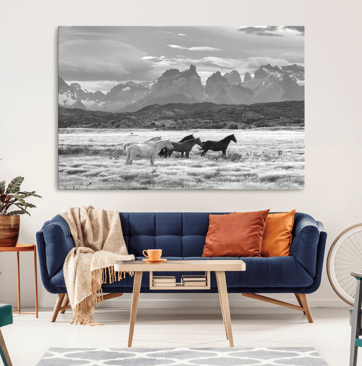 A black and white landscape of wild horses grazing in a vast grassland with towering mountains in the background, creating a moody and rustic western aesthetic.