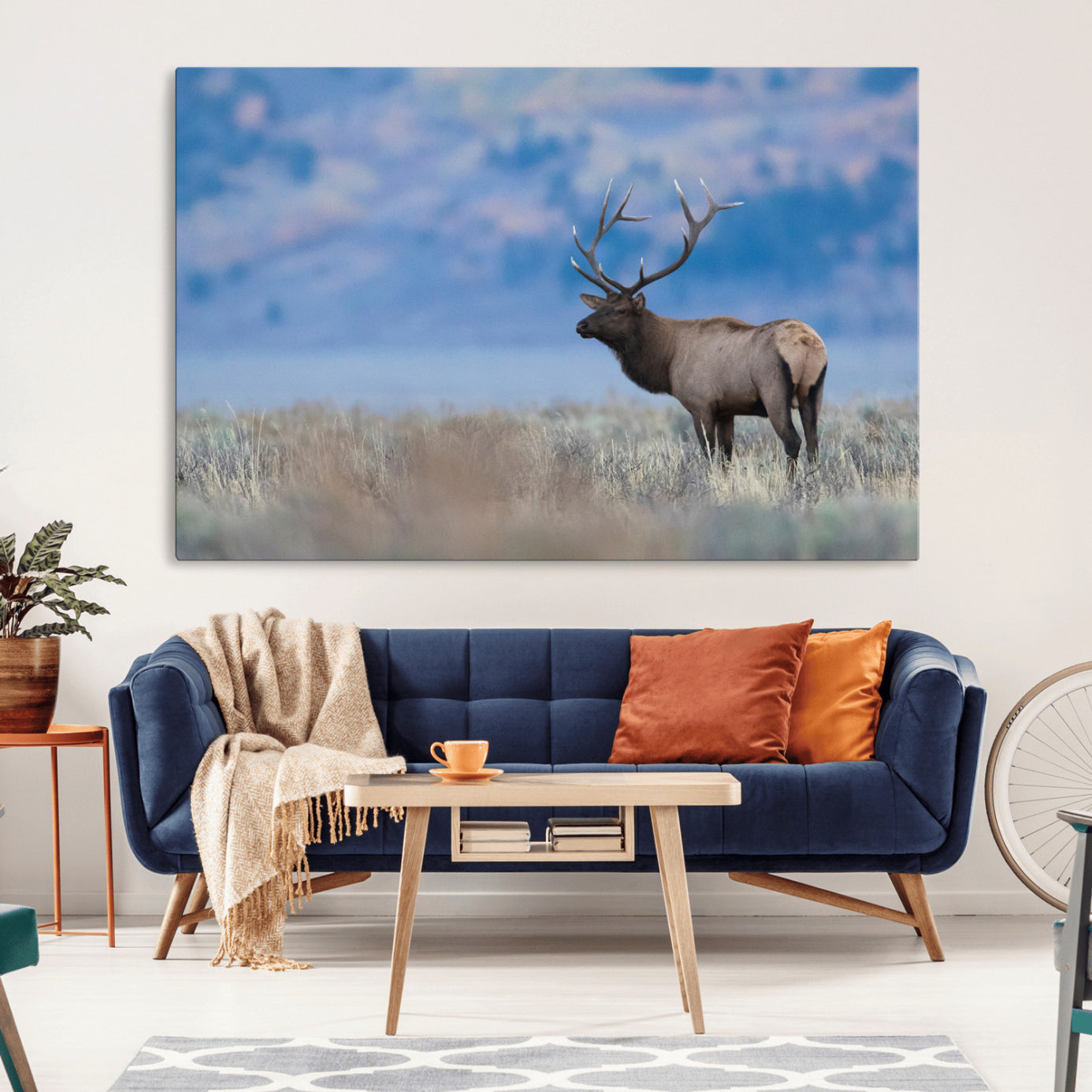 Elk with large antlers standing in open field, mountains blurred in background, perfect for rustic cabin or lodge-style decor.