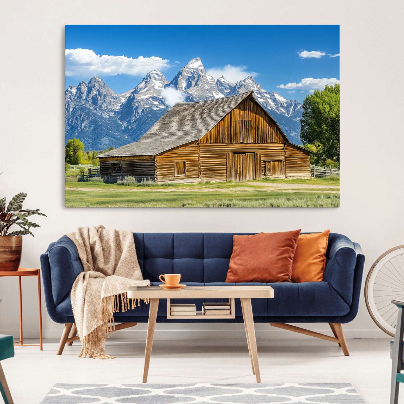 A rustic wooden barn sits in front of towering mountain peaks under a clear blue sky, perfect for farmhouse or cabin style interiors.