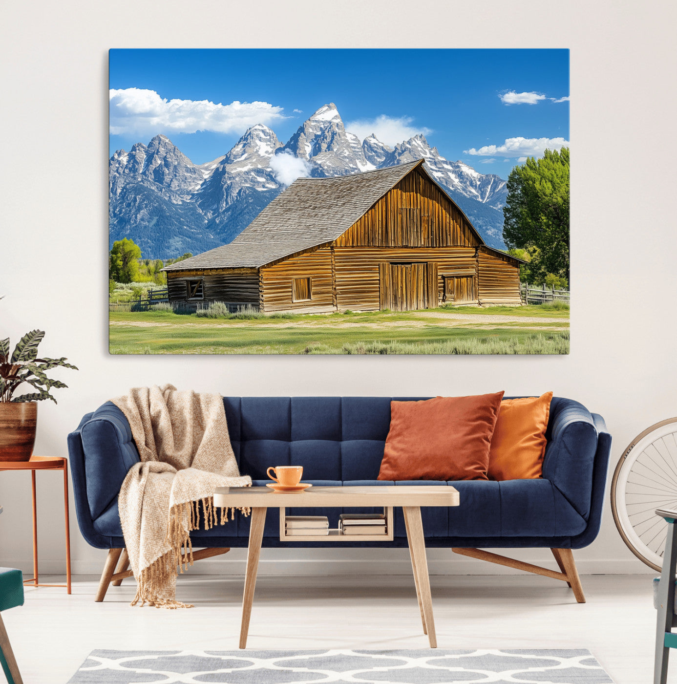A rustic wooden barn sits in front of towering mountain peaks under a clear blue sky, perfect for farmhouse or cabin style interiors.