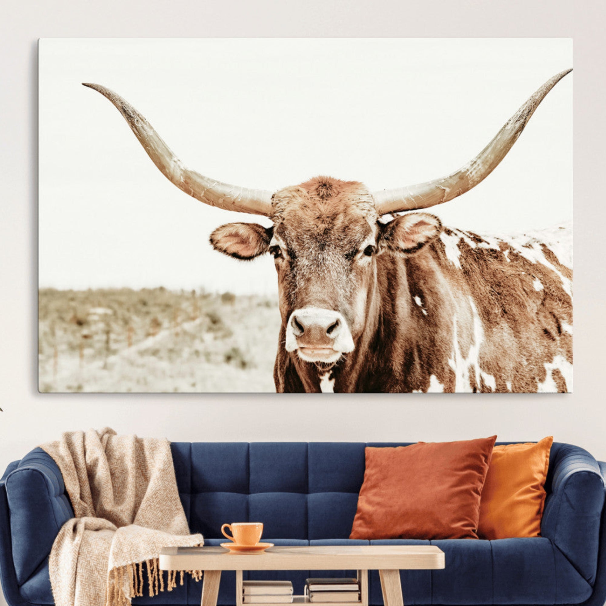 A Texas longhorn bull with wide horns, standing in a dry field under soft light, ideal for rustic farmhouse or western-themed interiors.