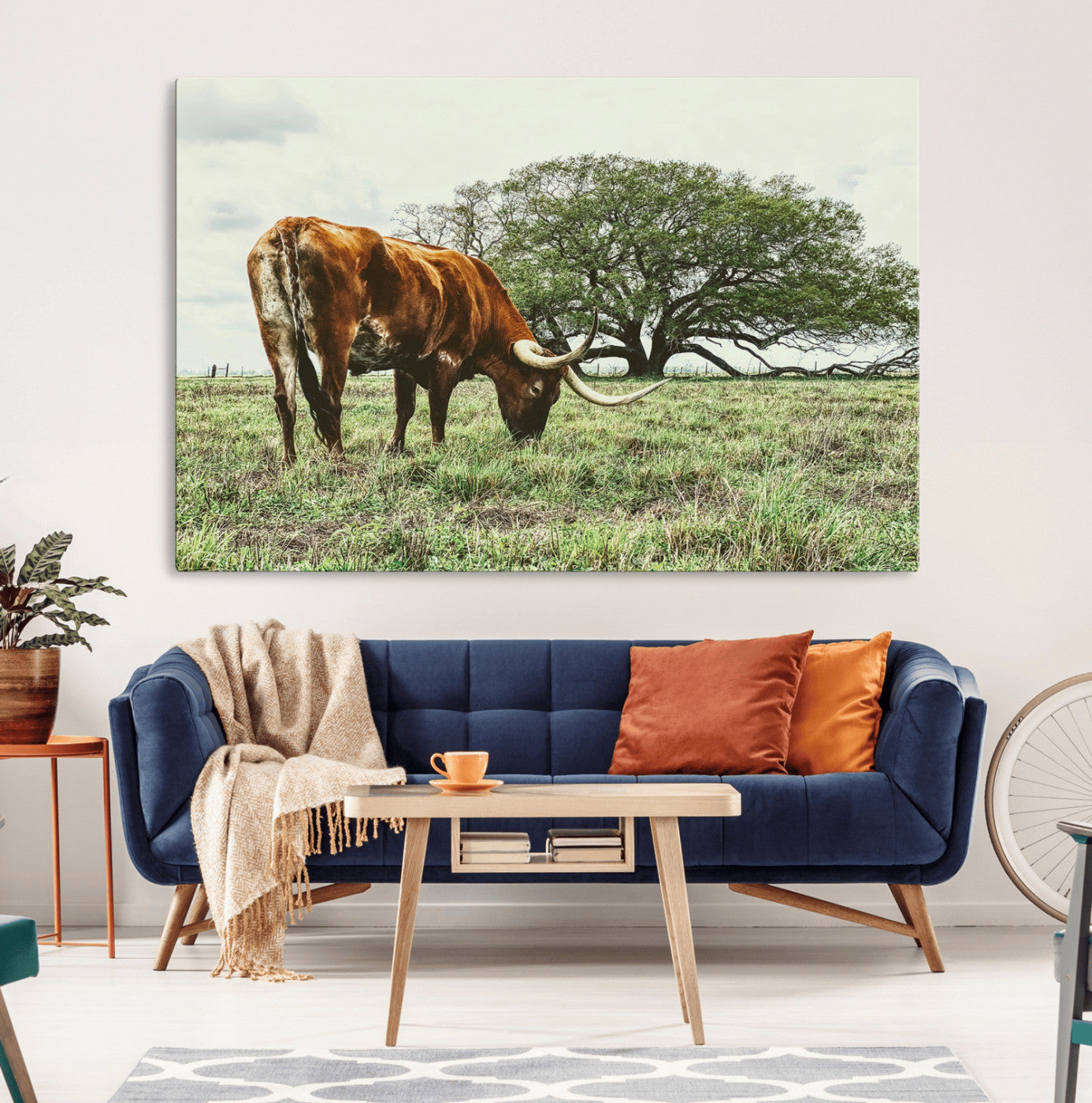 A Texas Longhorn grazing in a green pasture with a large tree in the background, evoking a rustic Western and farmhouse aesthetic.