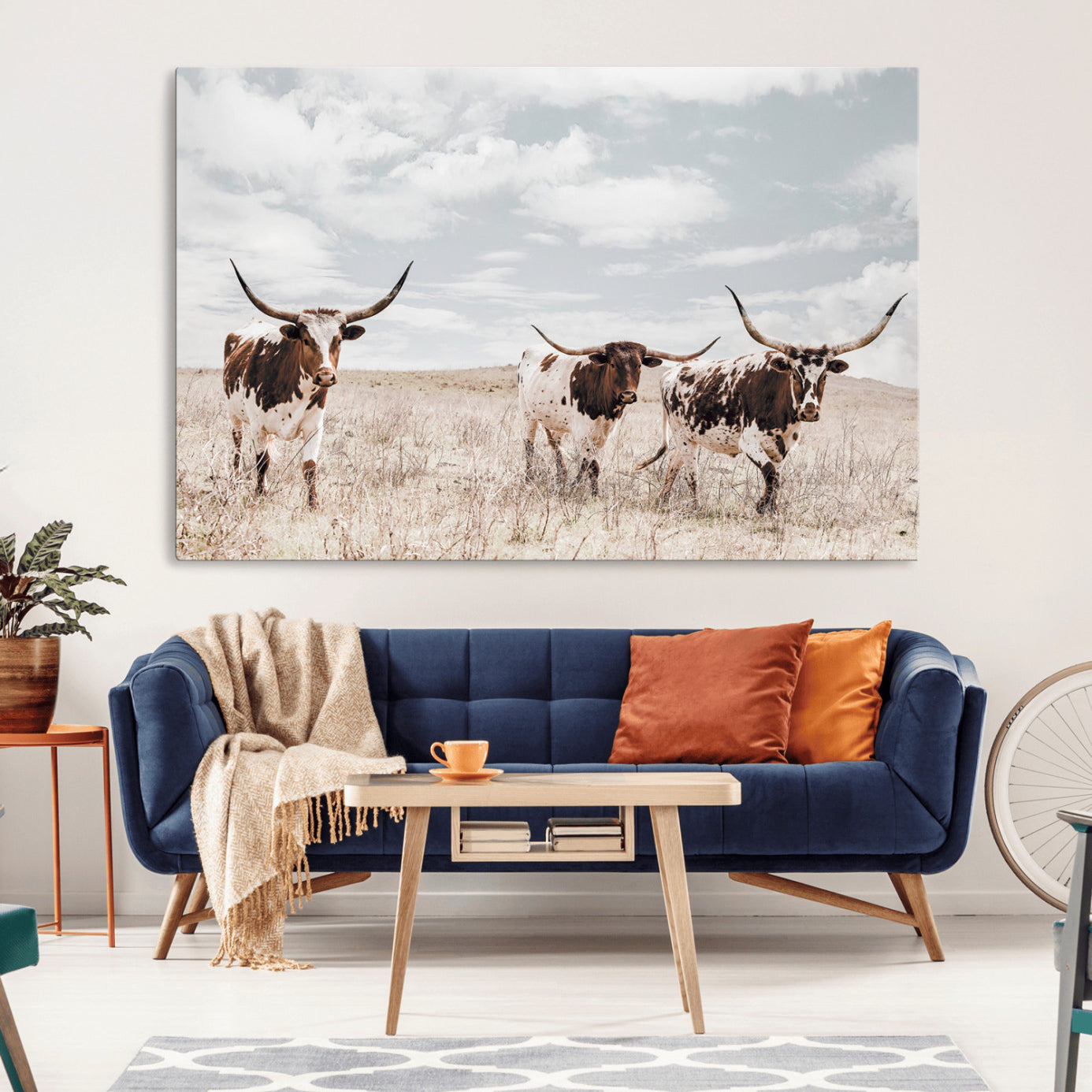 Three Texas Longhorn cattle walking through a dry grassy field under a partly cloudy sky.