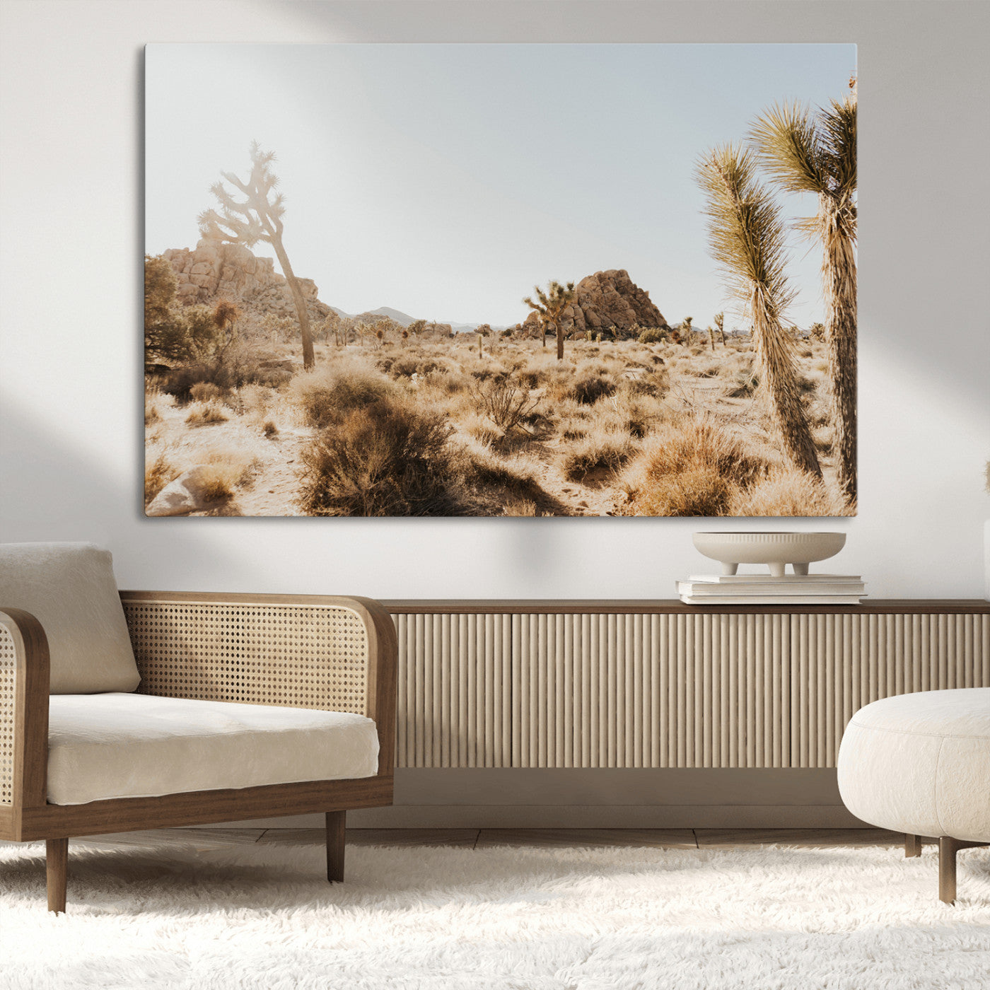Sunlit desert landscape featuring Joshua trees, rocky formations, and dry bushes under a clear sky.