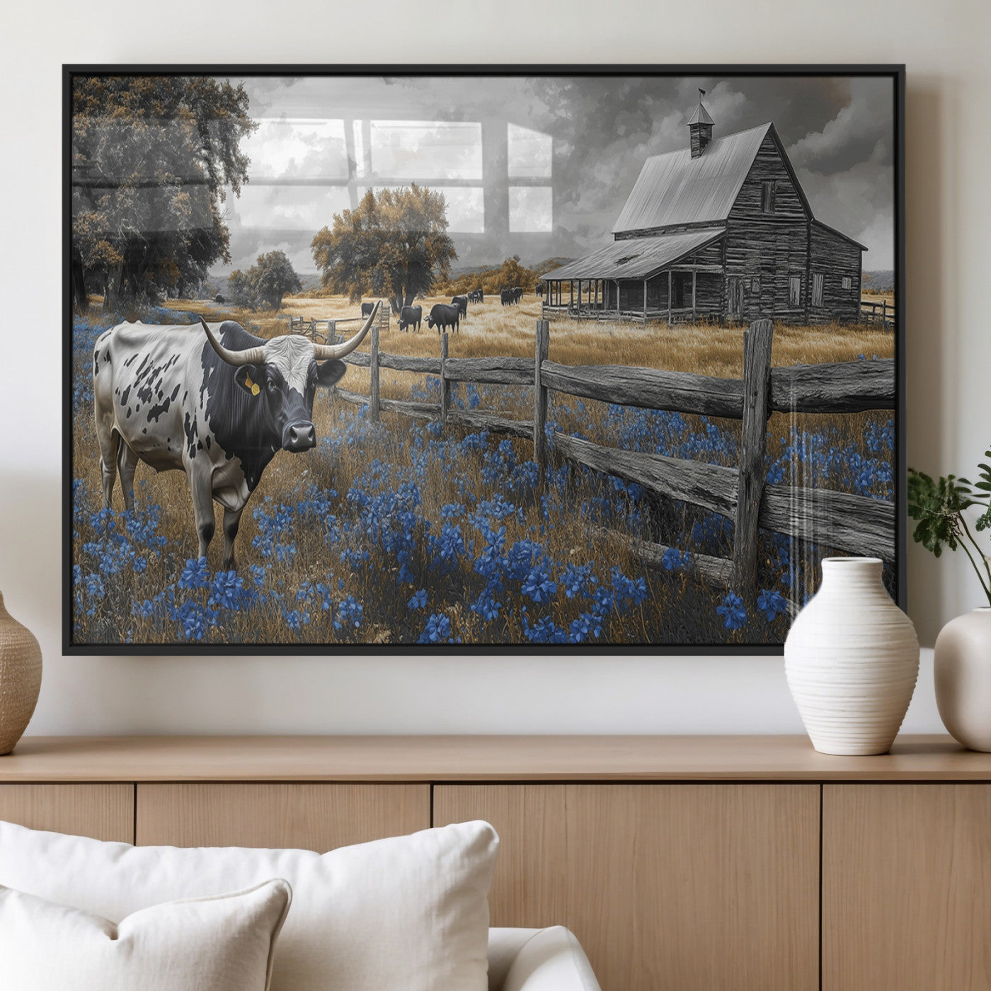 A Texas longhorn stands in front of a rustic barn and wooden fence, with bluebonnets and grazing cattle under dramatic skies.
