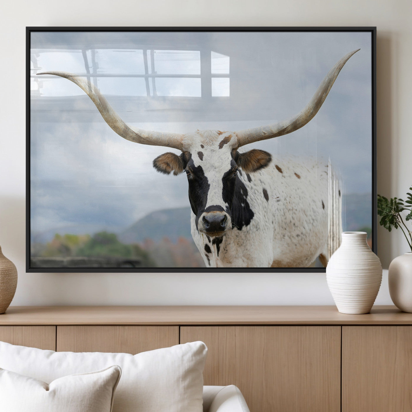Close-up of a Texas Longhorn with curved horns, black and white markings, set against a cloudy sky and distant hills, perfect for rustic decor.