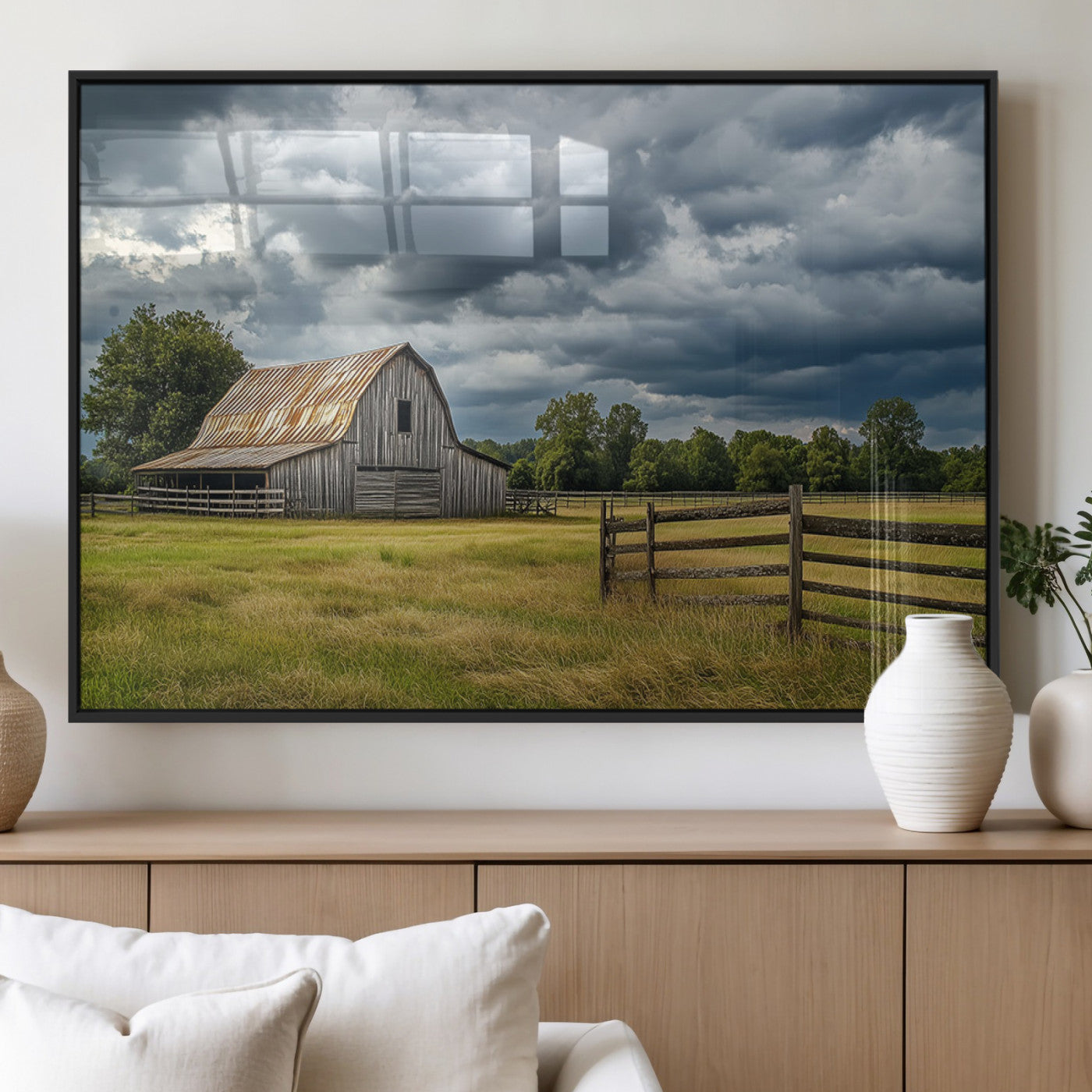 "Rustic barn in a wide open field under a dramatic sky with dark clouds, surrounded by a wooden fence and lush green trees."
