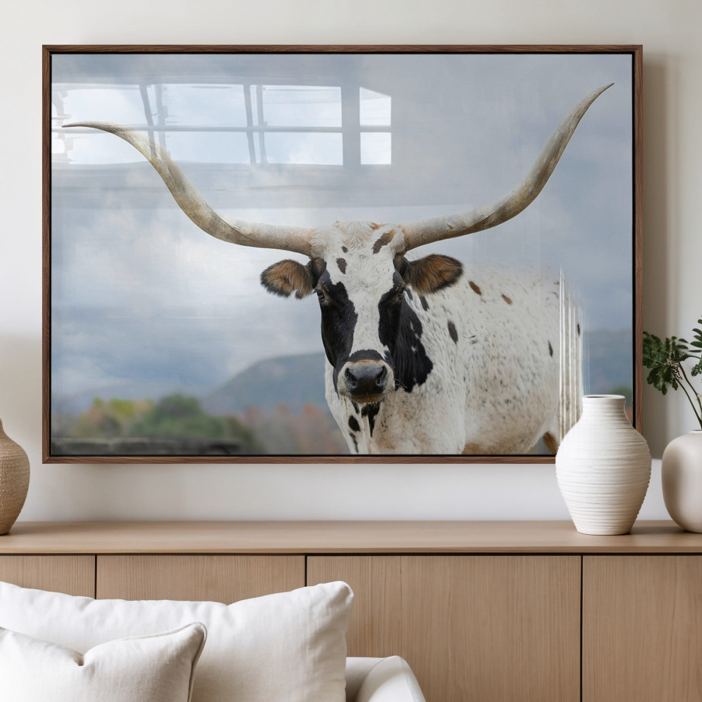 Close-up of a Texas Longhorn with curved horns, black and white markings, set against a cloudy sky and distant hills, perfect for rustic decor.