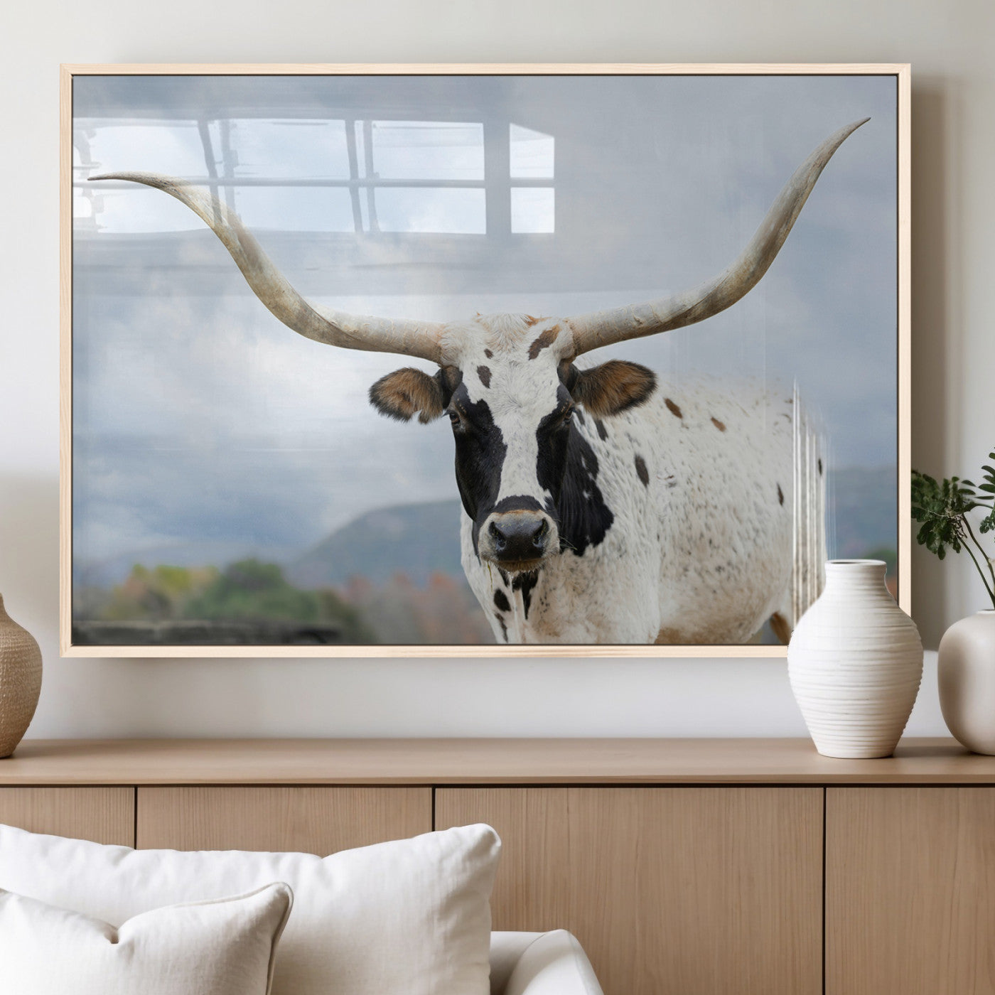 Close-up of a Texas Longhorn with curved horns, black and white markings, set against a cloudy sky and distant hills, perfect for rustic decor.