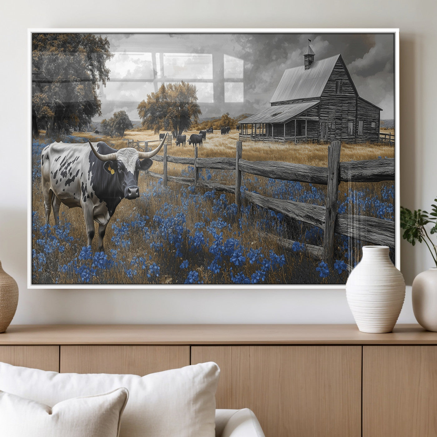A Texas longhorn stands in front of a rustic barn and wooden fence, with bluebonnets and grazing cattle under dramatic skies.