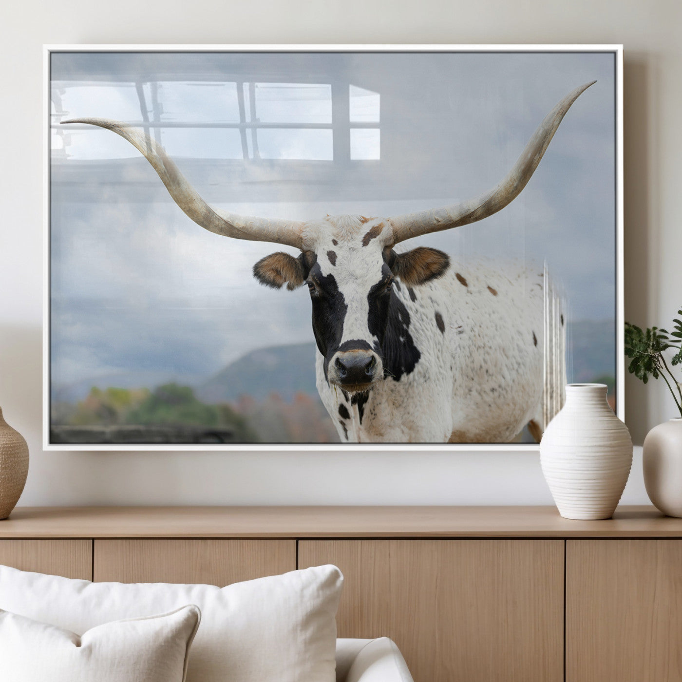 Close-up of a Texas Longhorn with curved horns, black and white markings, set against a cloudy sky and distant hills, perfect for rustic decor.
