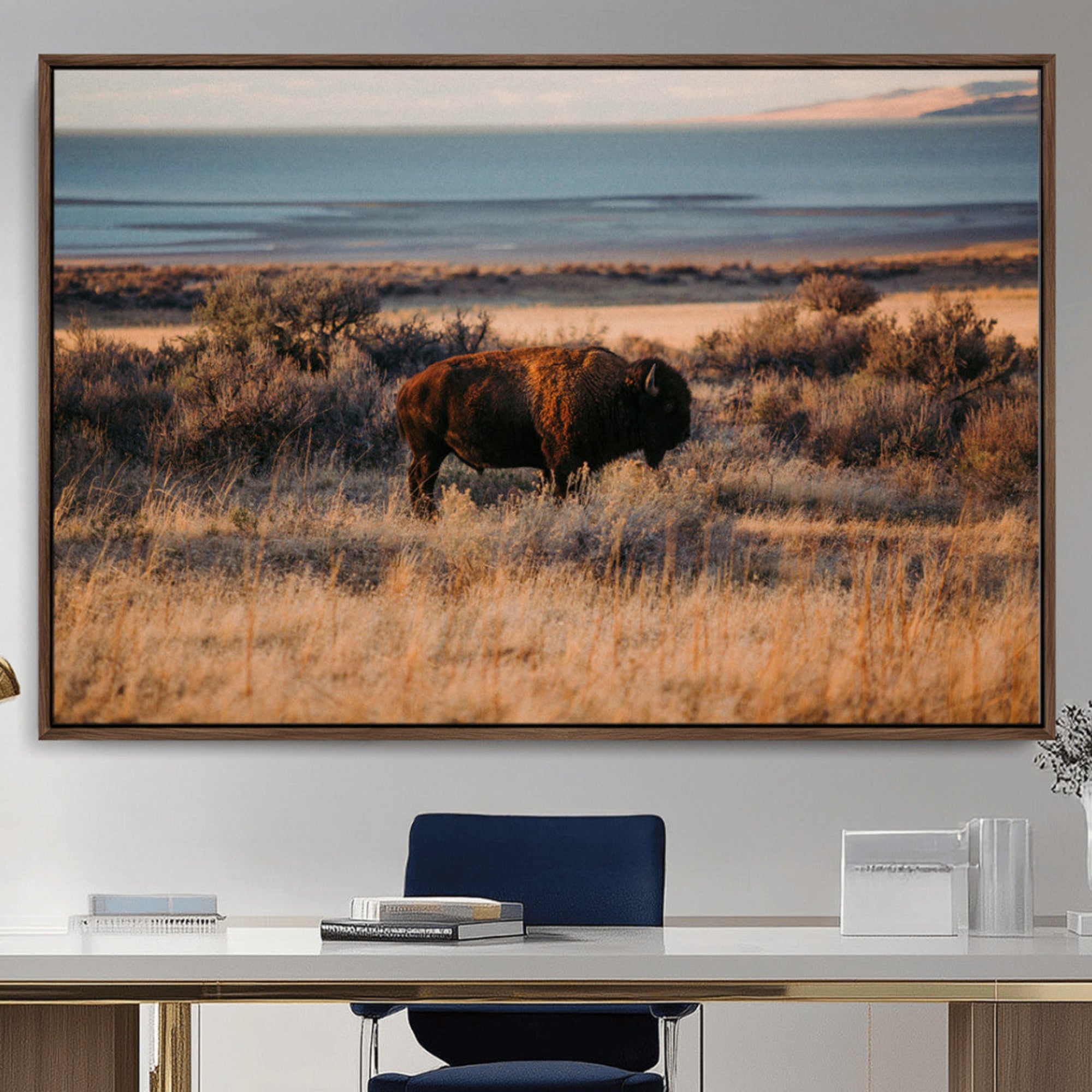 A lone bison grazing in golden prairie grass at sunset, with warm earthy tones and a distant lake view, perfect for rustic and western decor.