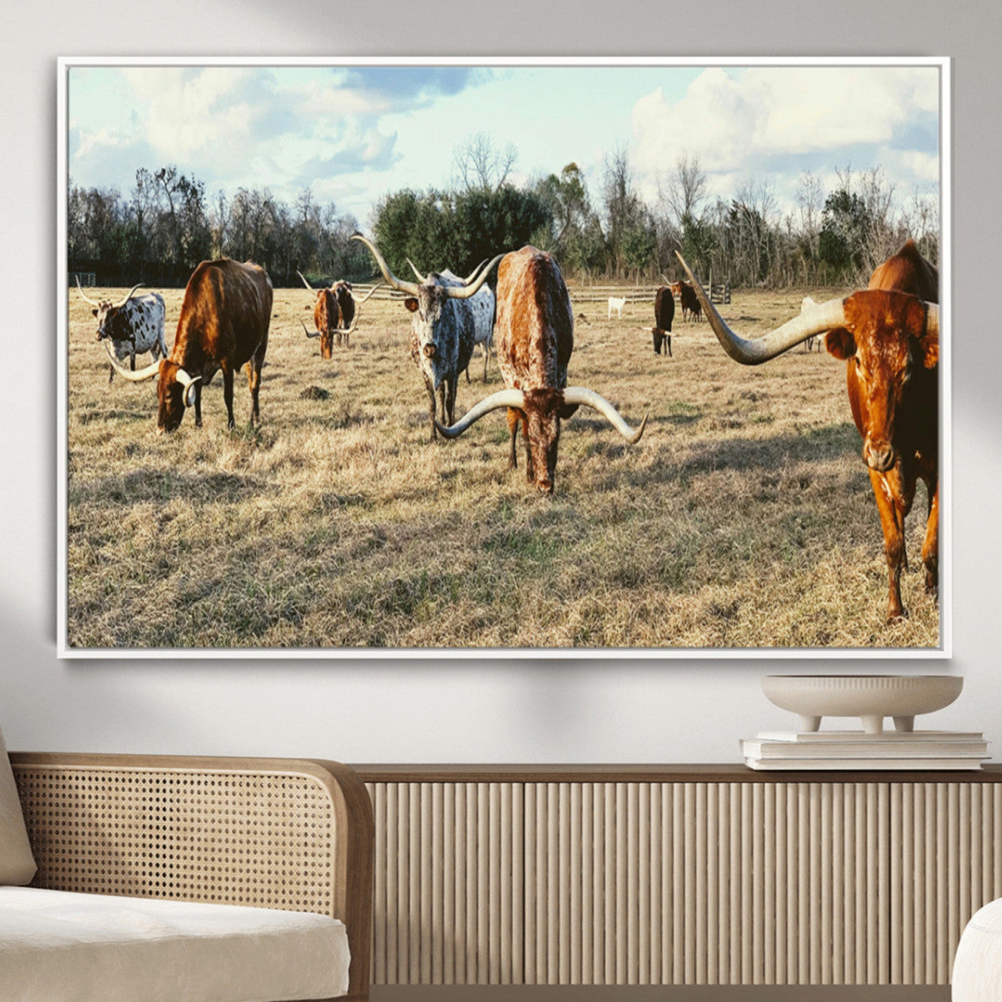 A herd of Texas Longhorn cattle grazing in an open field under a partly cloudy sky, capturing a rustic and Western ranch aesthetic.