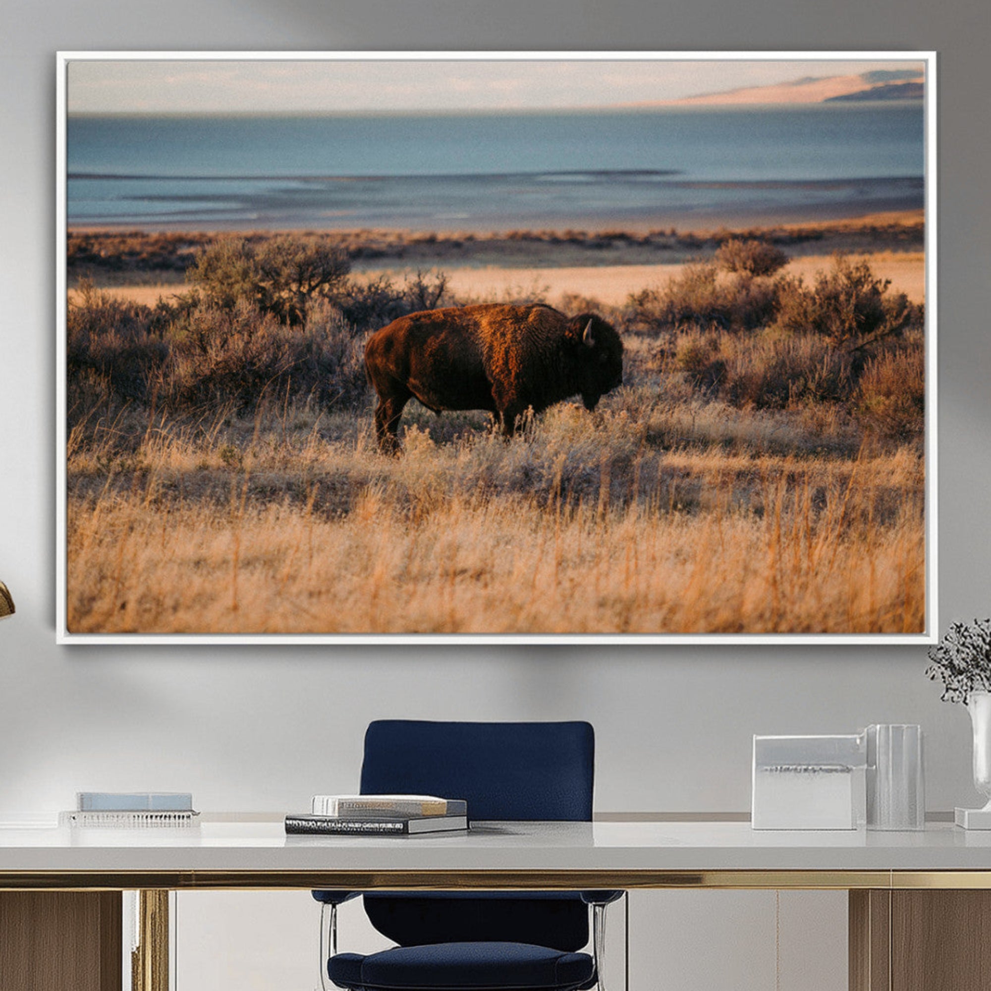 A lone bison grazing in golden prairie grass at sunset, with warm earthy tones and a distant lake view, perfect for rustic and western decor.