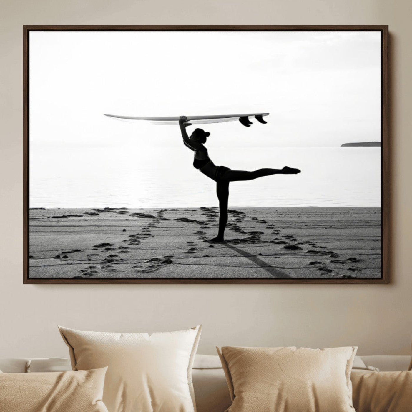A woman balances a surfboard on her head while striking a yoga pose on the beach, silhouetted against a calm ocean horizon.