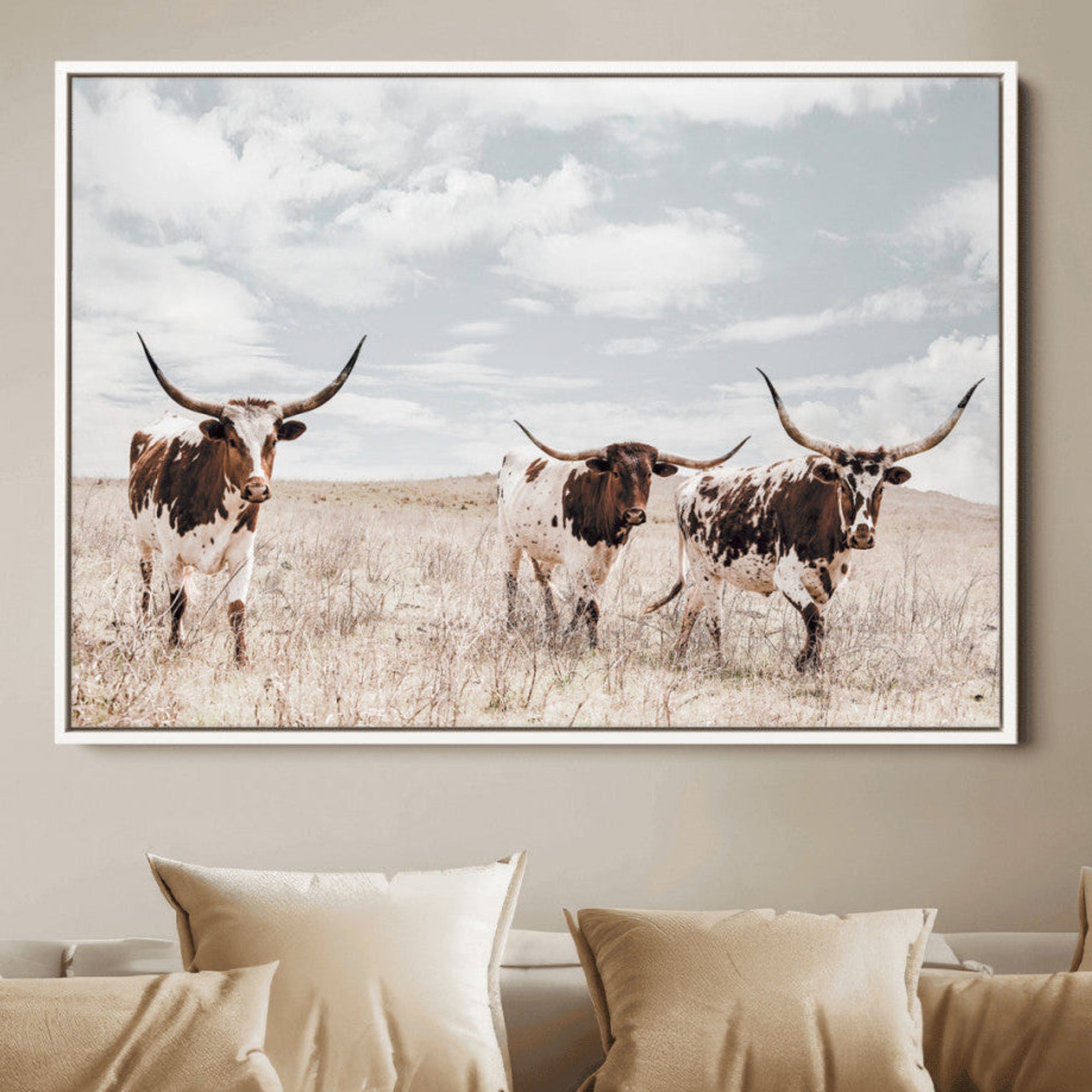 Three Texas Longhorn cattle walking through a dry grassy field under a partly cloudy sky.