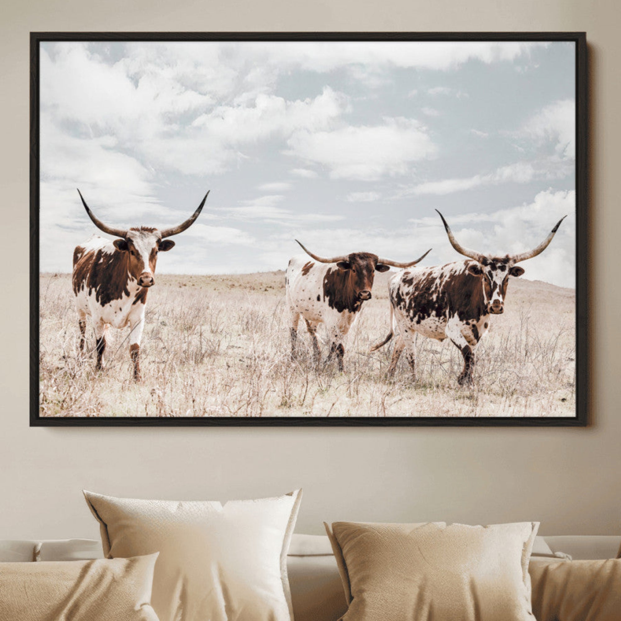 Three Texas Longhorn cattle walking through a dry grassy field under a partly cloudy sky.
