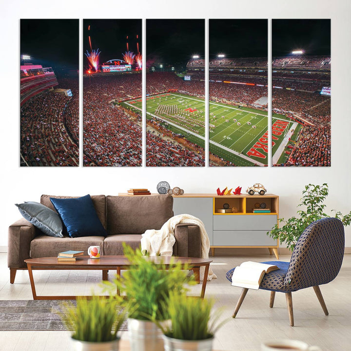 The University of Nebraska Cornhuskers Football Team Print, featuring Lincoln Memorial Stadium in a vibrant triptych canvas with fireworks above and a gallery-quality finish, is elegantly displayed.