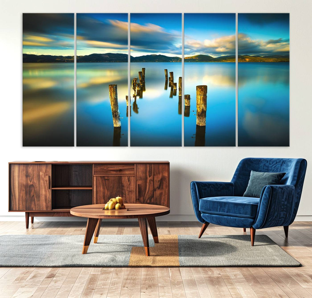 A triptych of a serene lake scene with old wooden pillars, blue sky, and clouds casts a coastal ambiance. The Sea Ocean Sunset Beach Wall Art Canvas Print reflects the soothing nature of the ocean.