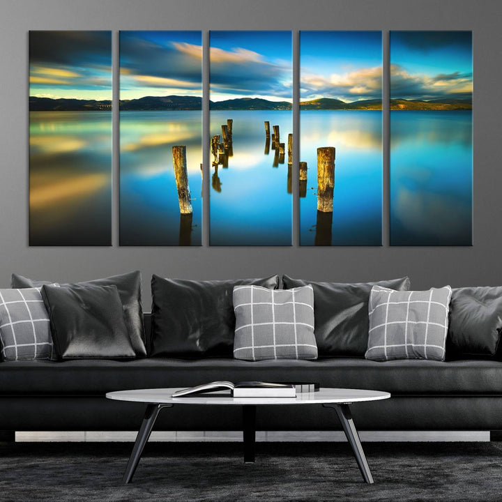 A triptych of a serene lake scene with old wooden pillars, blue sky, and clouds casts a coastal ambiance. The Sea Ocean Sunset Beach Wall Art Canvas Print reflects the soothing nature of the ocean.