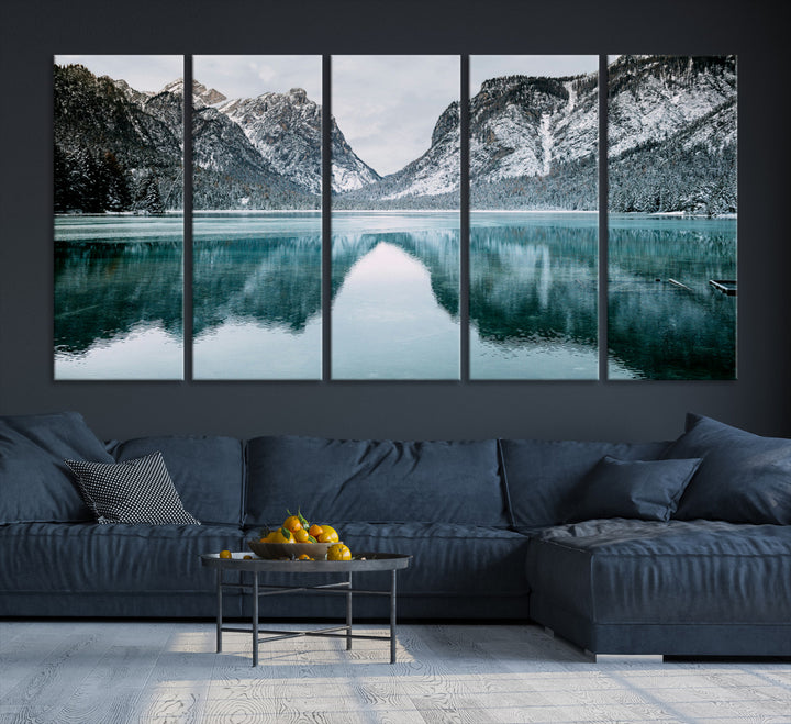 Crystal-clear alpine lake reflecting snow-covered mountains, surrounded by evergreen trees, creating a serene and tranquil winter landscape.
