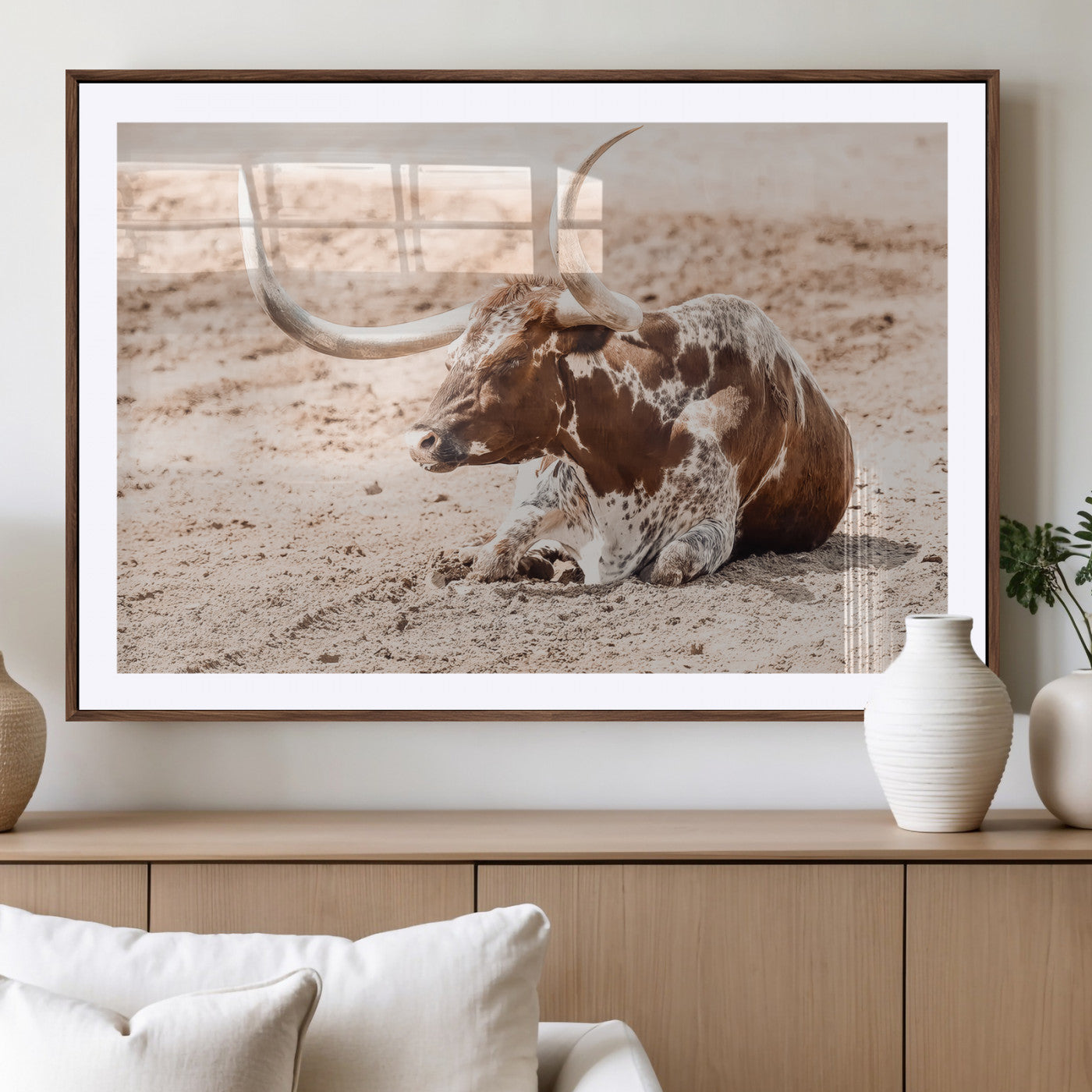 Texas Longhorn bull resting on dusty ground with warm tones, ideal for rustic western or farmhouse-themed wall decor.