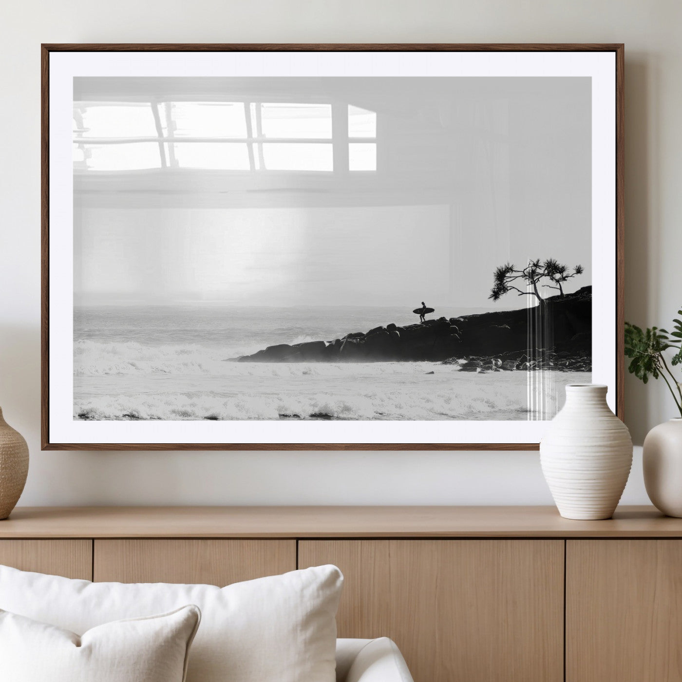Black and white photo of a surfer standing on rocky cliffs, gazing at the waves, embodying the spirit of adventure and solitude.