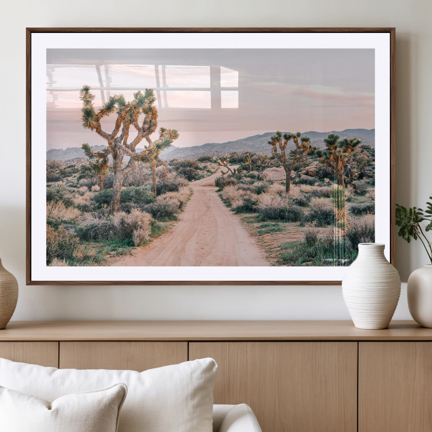 A dusty road winding through Joshua Tree National Park, framed by iconic twisted trees and warm desert tones under a soft pastel sky.