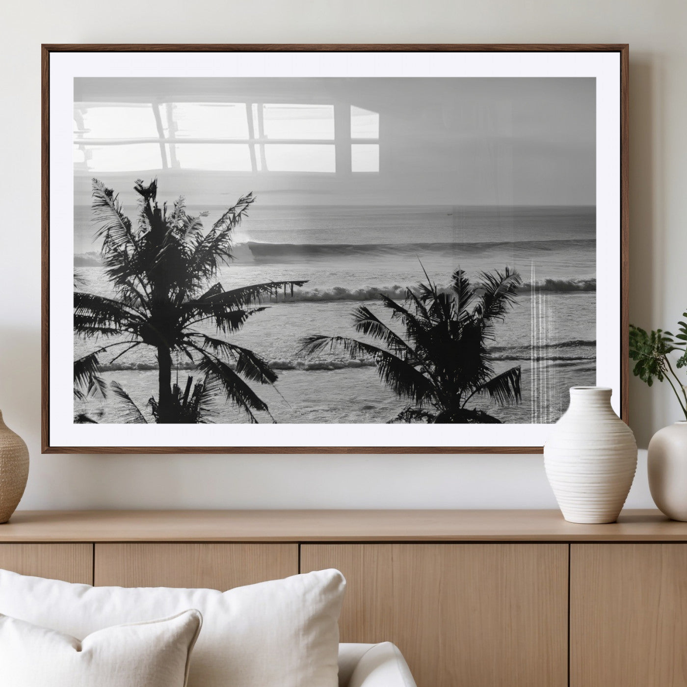 Black and white view of ocean waves crashing on a tropical coastline, framed by silhouetted palm trees under a vast, open sky.