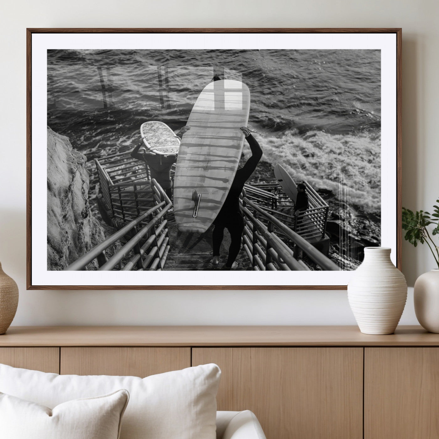 Black and white photo of surfers carrying boards down a rugged cliffside stairway, capturing a bold and adventurous coastal scene.