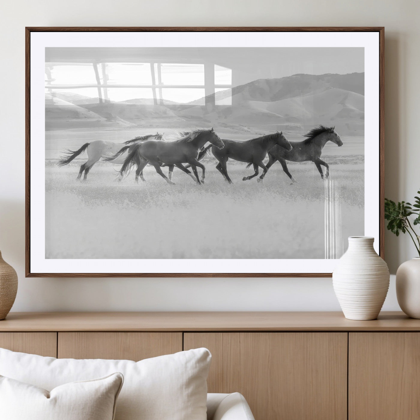 A black and white image of wild horses running freely across an open grassland, capturing the power and beauty of untamed nature in a rustic western setting.