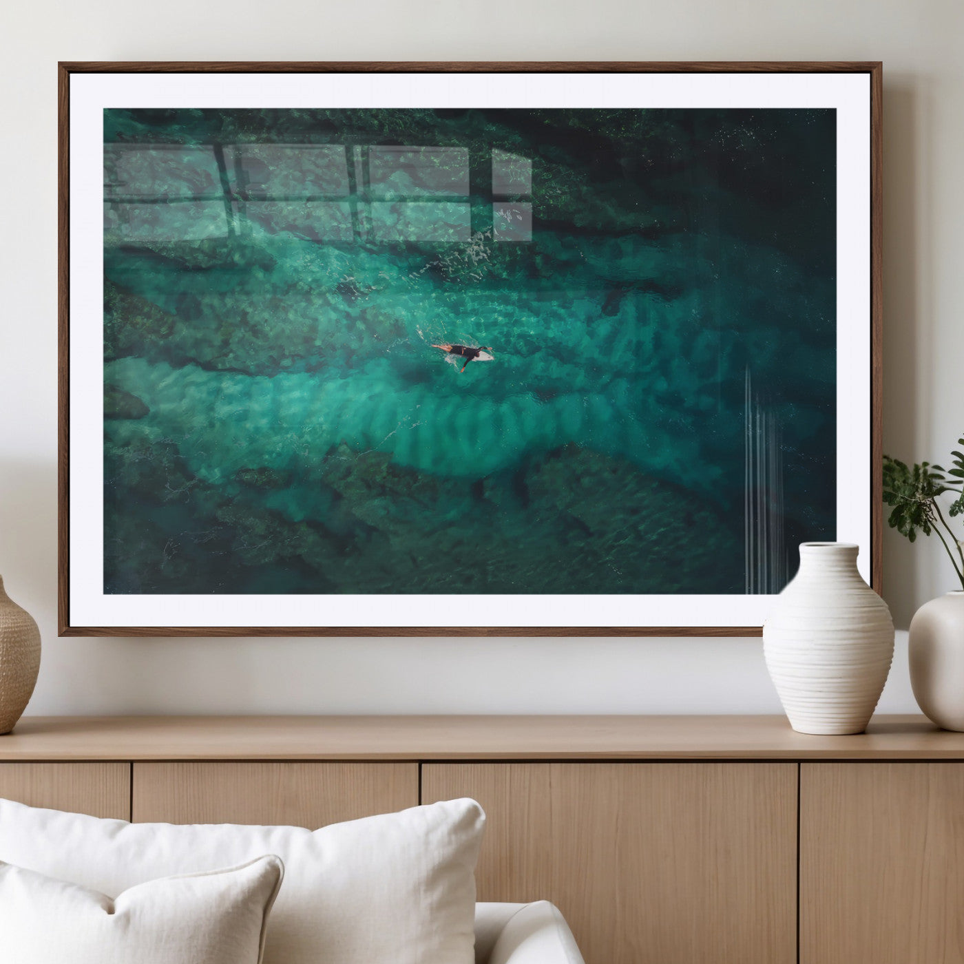 An aerial view of a solo surfer paddling through crystal-clear turquoise waters over a sunlit reef, capturing the beauty and serenity of open water surfing.