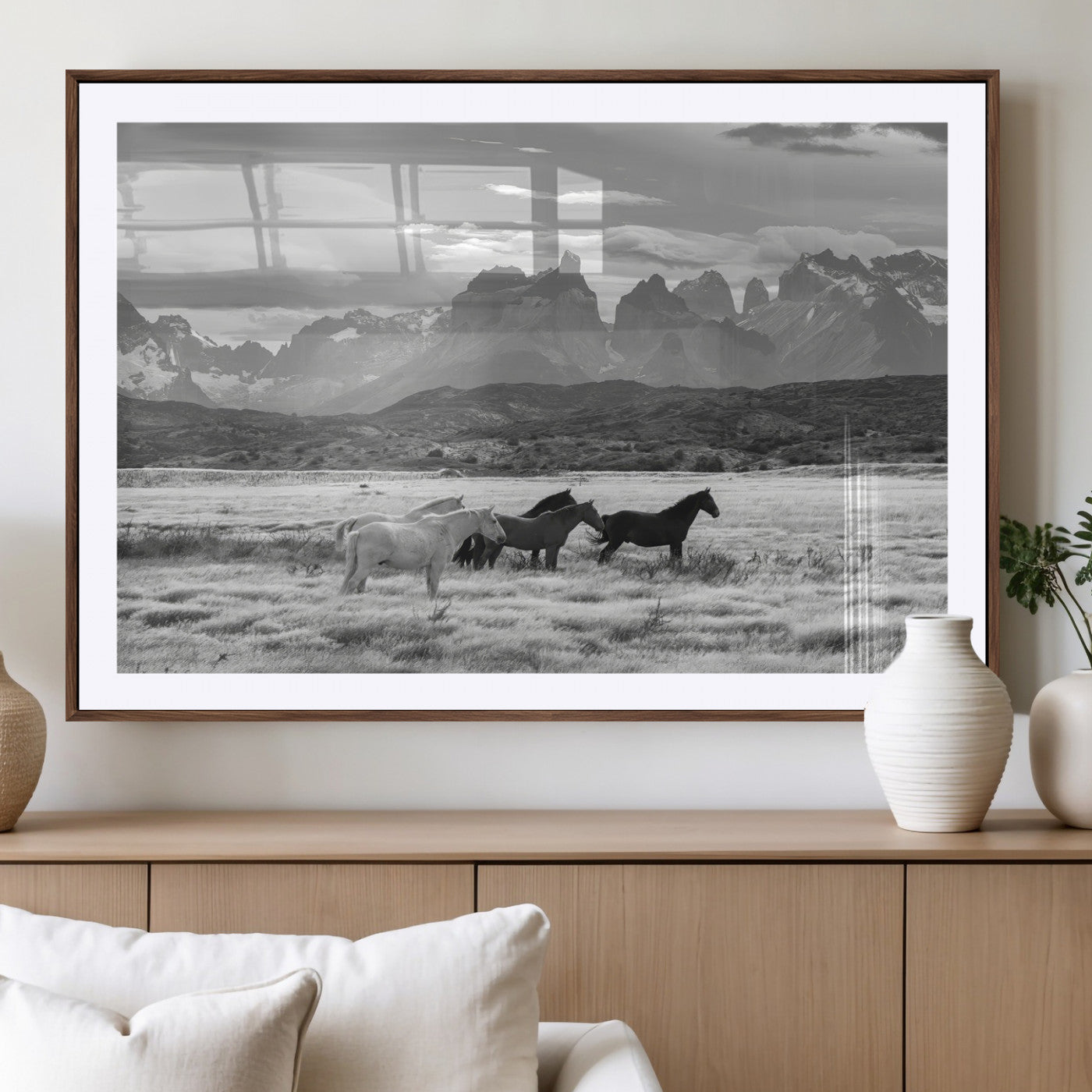 A black and white landscape of wild horses grazing in a vast grassland with towering mountains in the background, creating a moody and rustic western aesthetic.