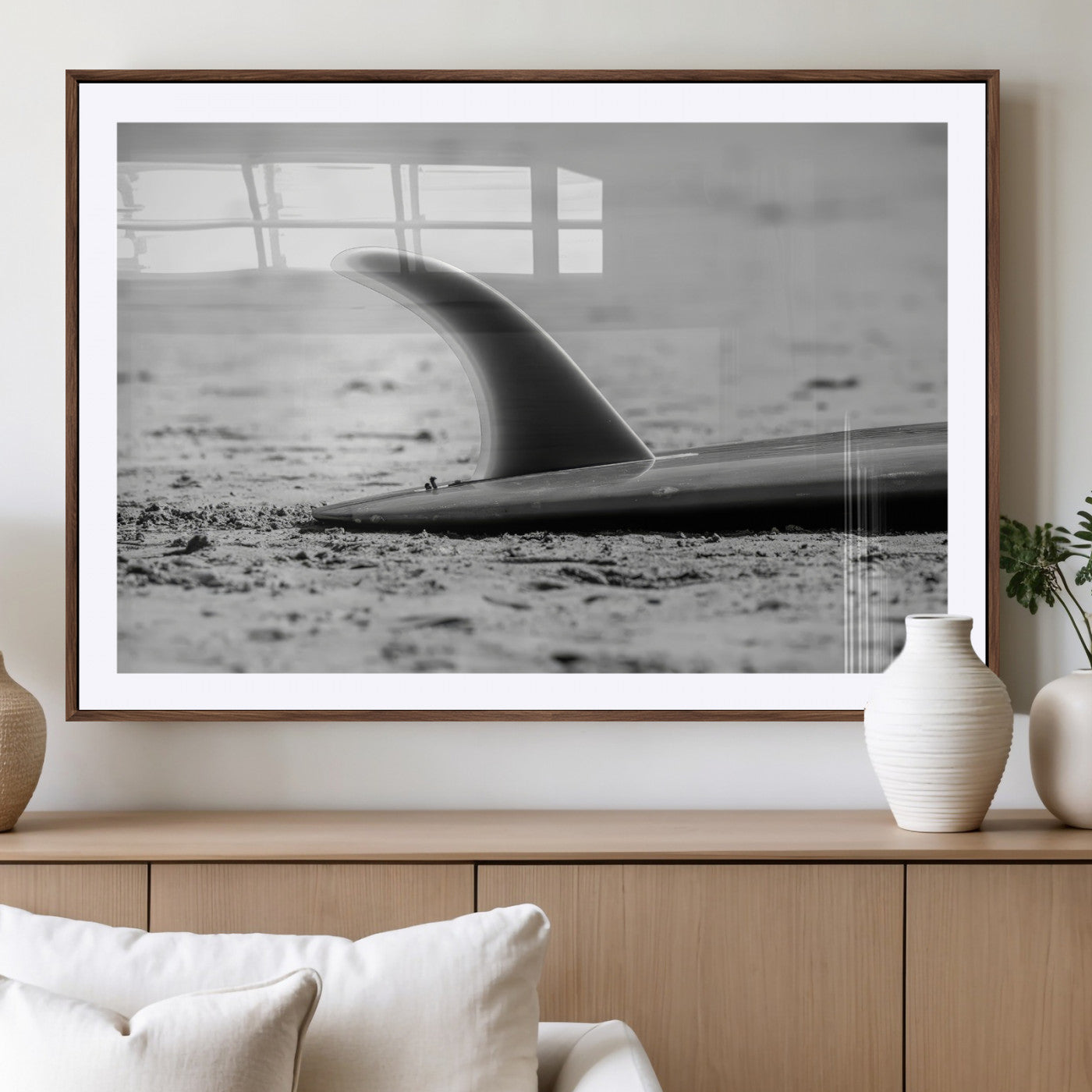 A black and white close-up of a surfboard fin resting on the sandy shore, highlighting minimalist beach aesthetics and classic surf culture.