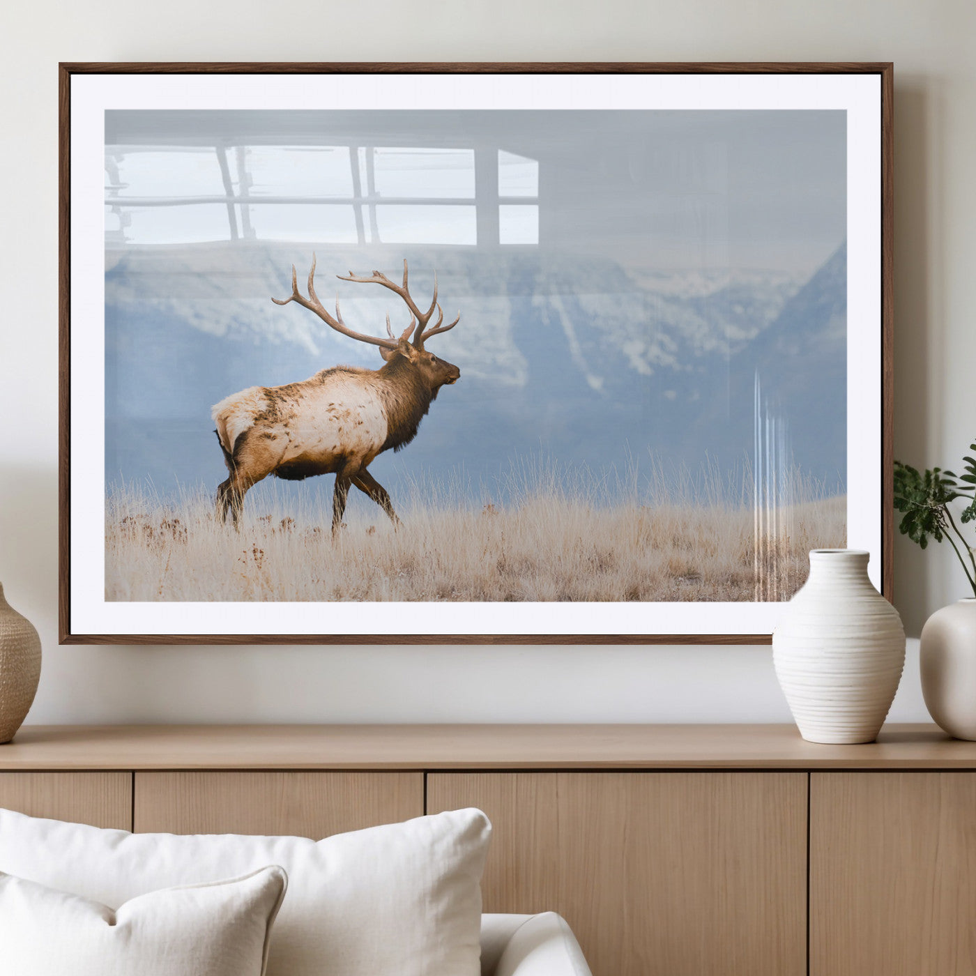 An elk walking on snowy grassland with majestic mountains in the background, ideal for rustic lodge or cabin wall decor.