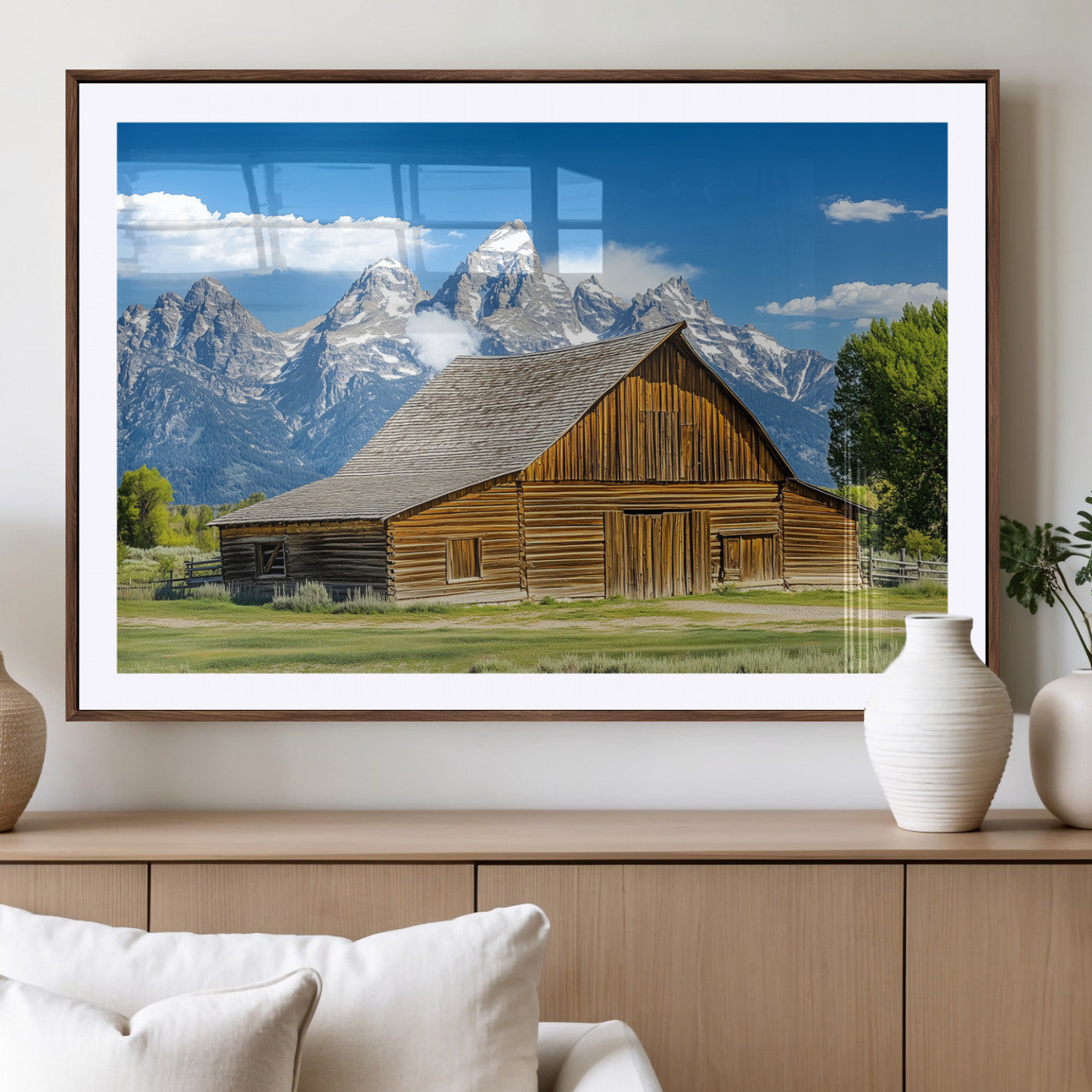 A rustic wooden barn sits in front of towering mountain peaks under a clear blue sky, perfect for farmhouse or cabin style interiors.